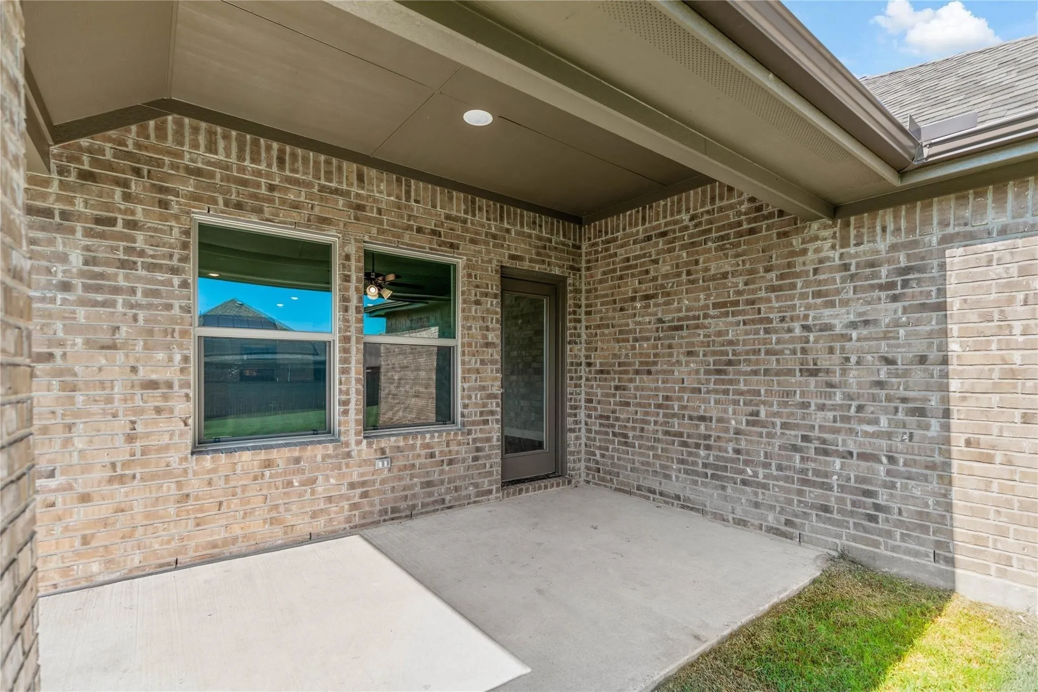 Covered patio with brick exterior, concrete slab, recessed lighting, and a glass-paneled door
