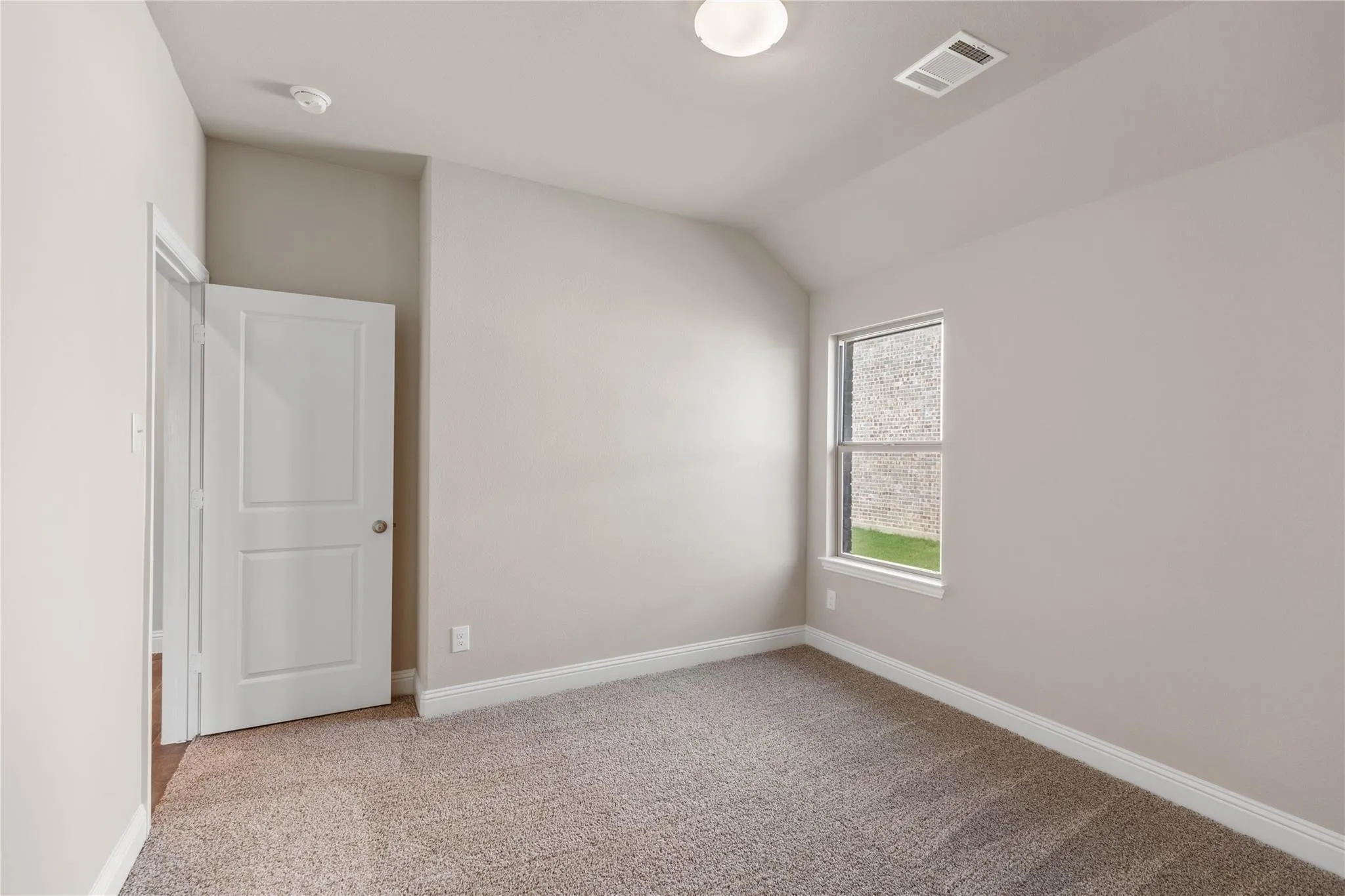 Vaulted ceiling, carpeted flooring, single window, white trim, and a white interior door