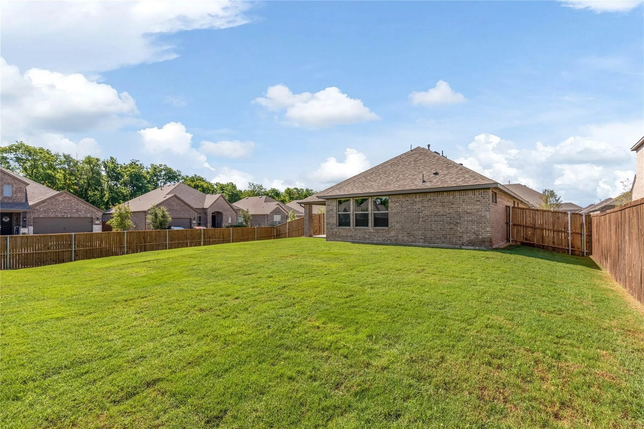 Expansive backyard featuring a manicured lawn, brick exterior, and a privacy fence
