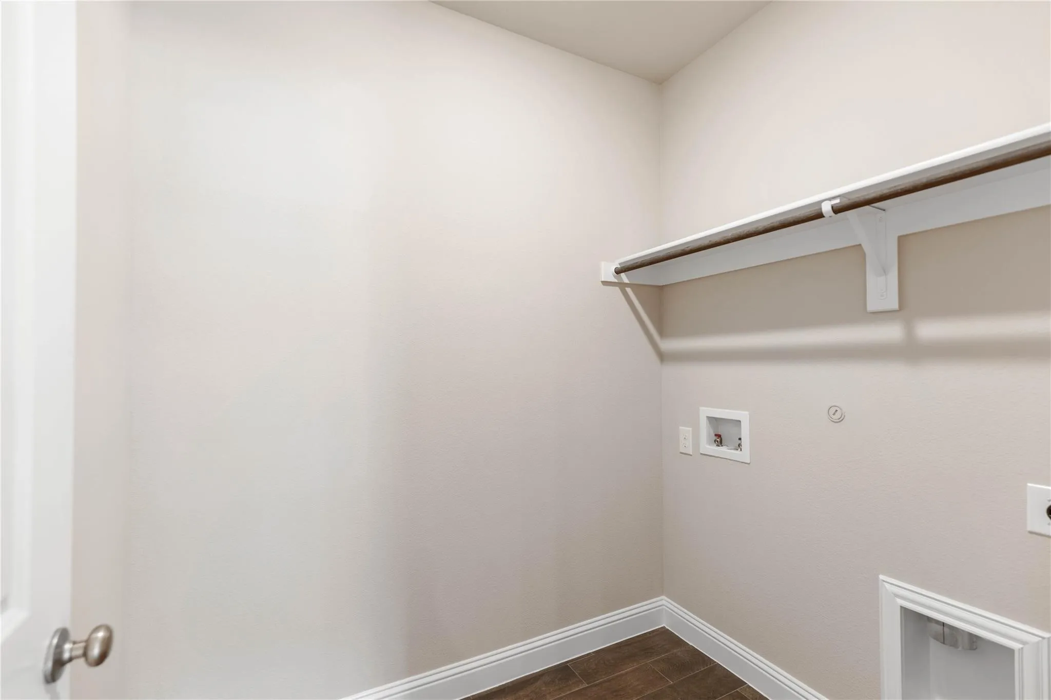 Laundry area with wood-finish flooring, white trim, and a built-in shelf with hanging rod