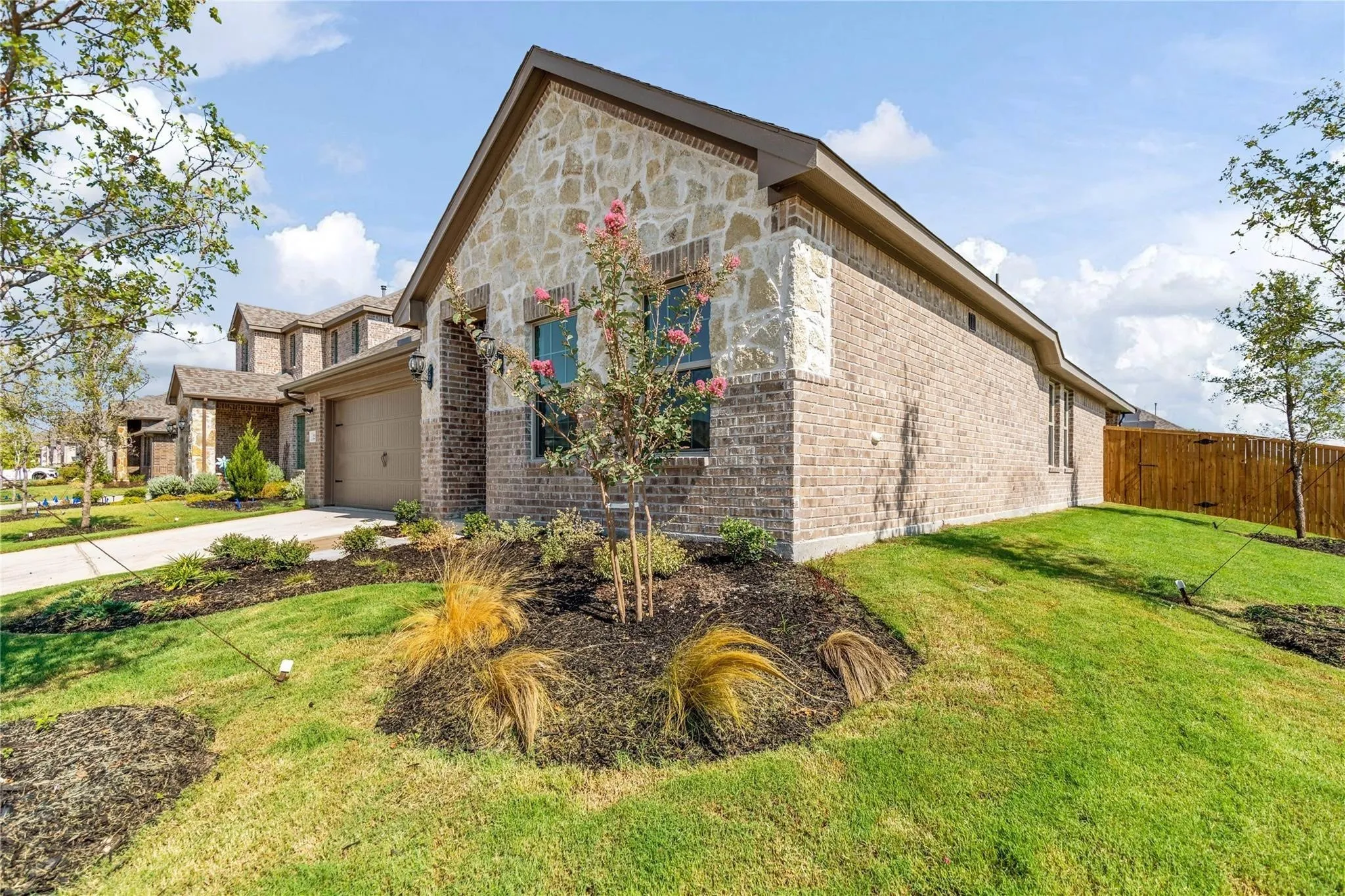 Stone and brick exterior with a pitched roof, attached garage, and landscaped front yard