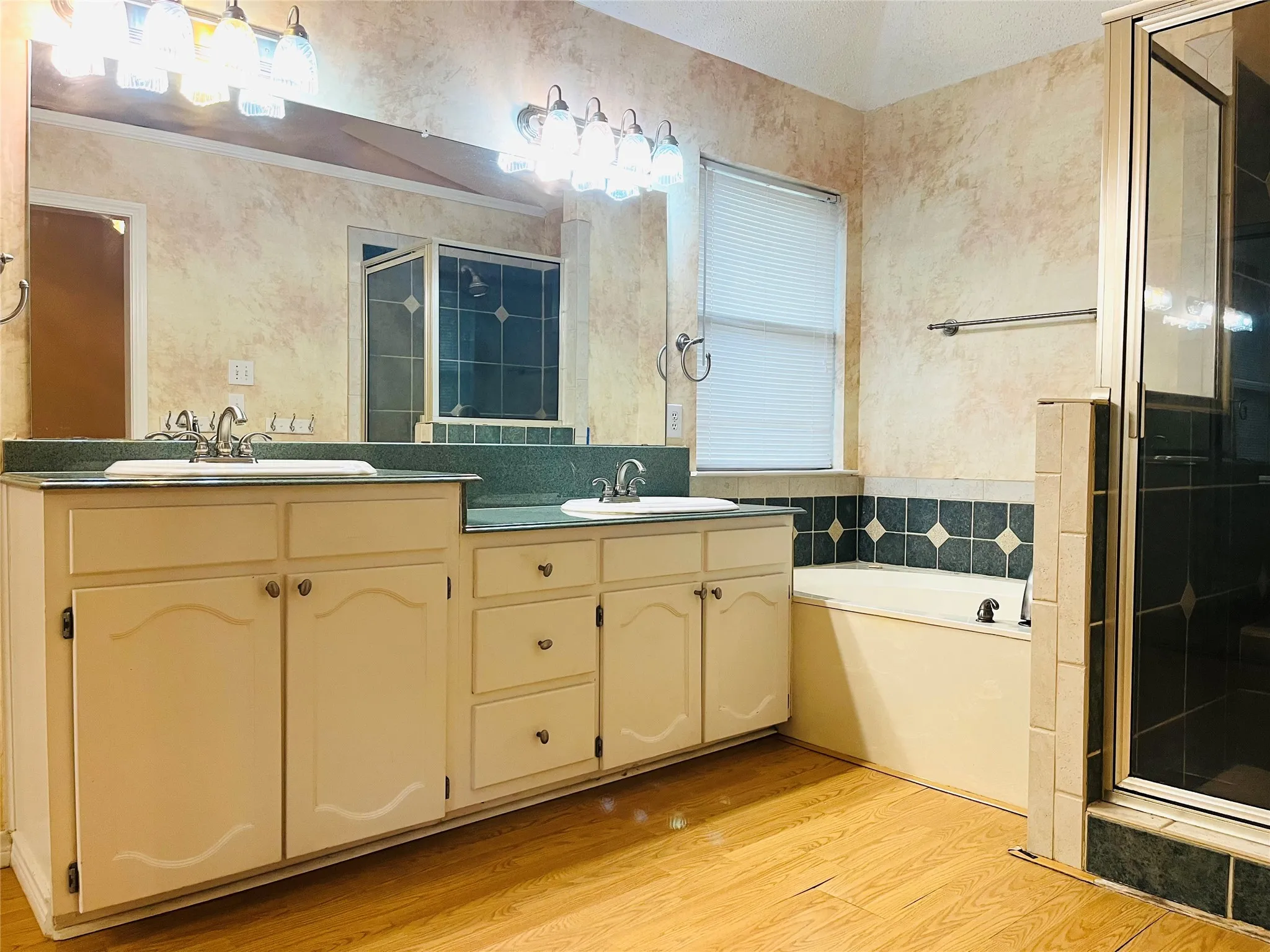 Dual vanity with integrated sinks, wood-finish flooring, built-in soaking tub, and enclosed shower with tile surround