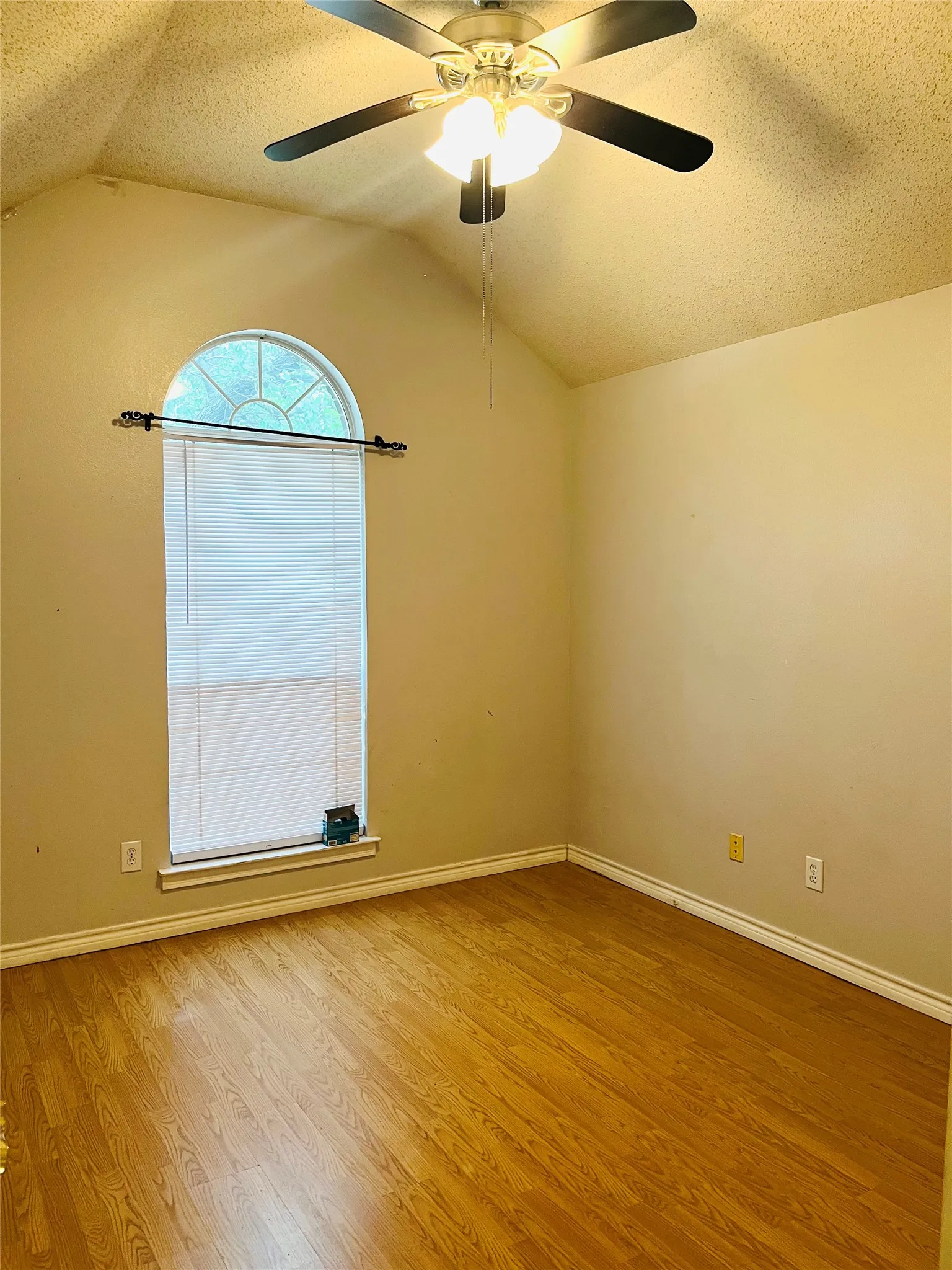 Vaulted ceiling with a ceiling fan, arched window, wood-finish flooring, and neutral wall tones