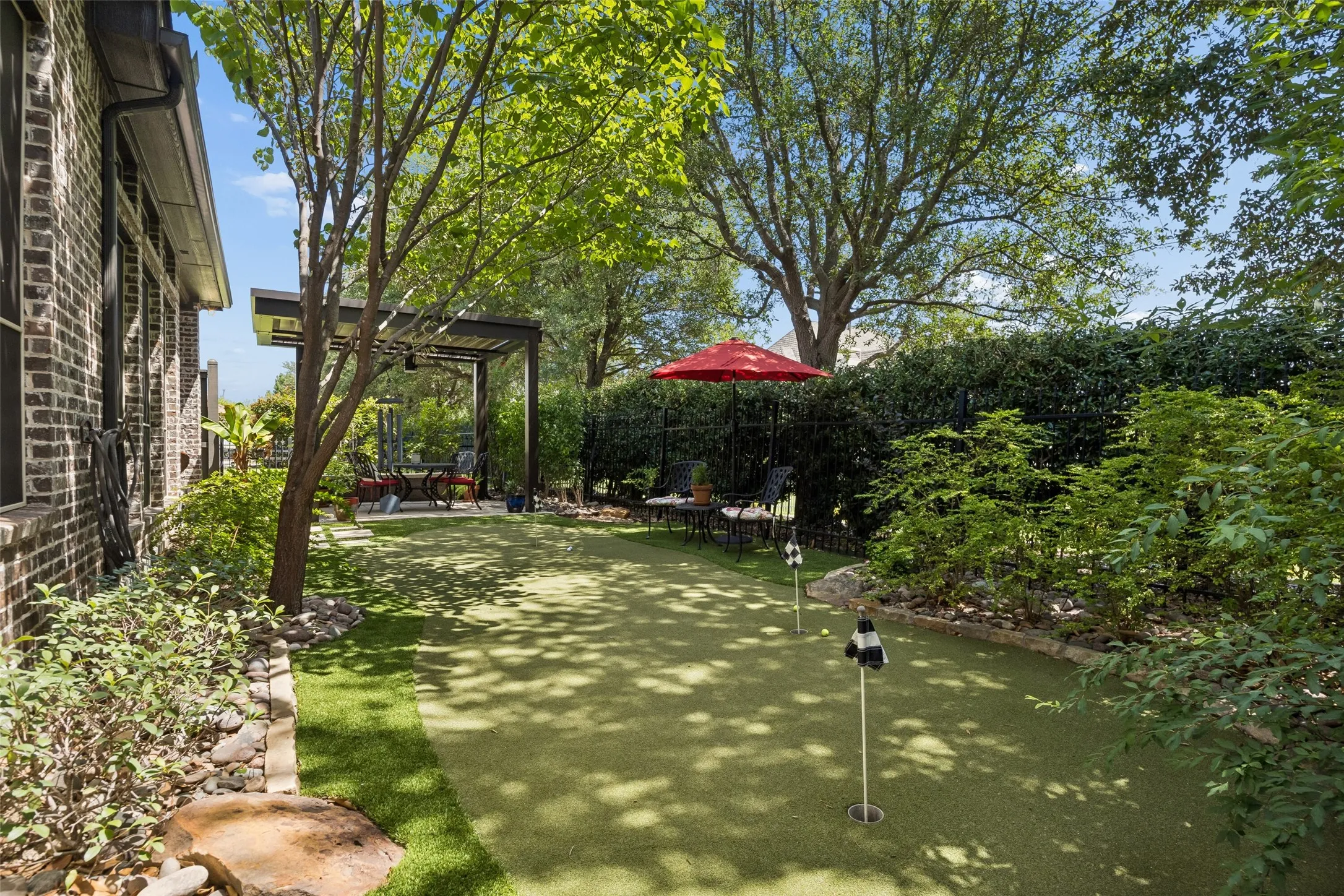Backyard retreat with a putting green and treed privacy fence line.