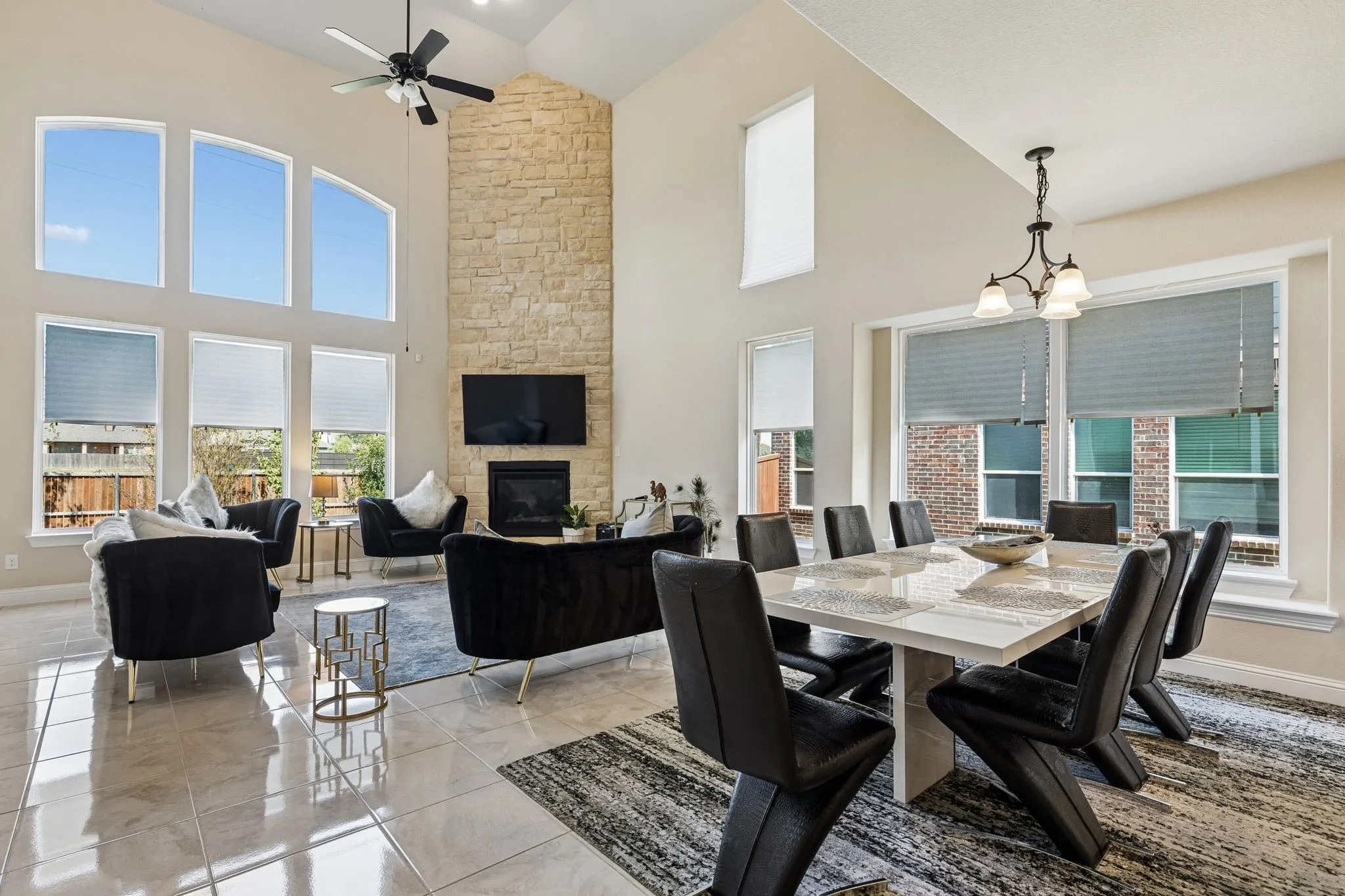 Vaulted ceiling with an integrated ceiling fan, stone-clad fireplace, large-format tile flooring, and multiple windows