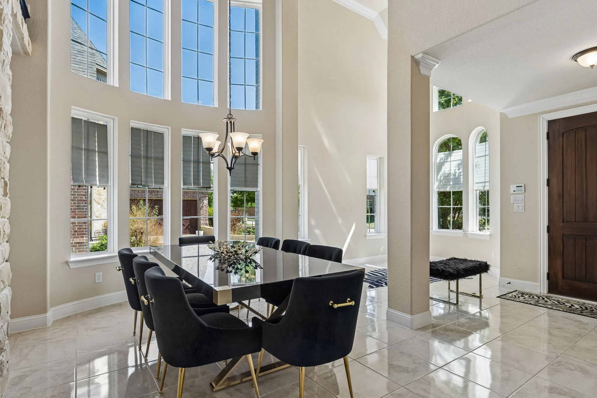 Two-story ceiling, multiple large windows, tile flooring, stone accent wall, and a solid wood entry door