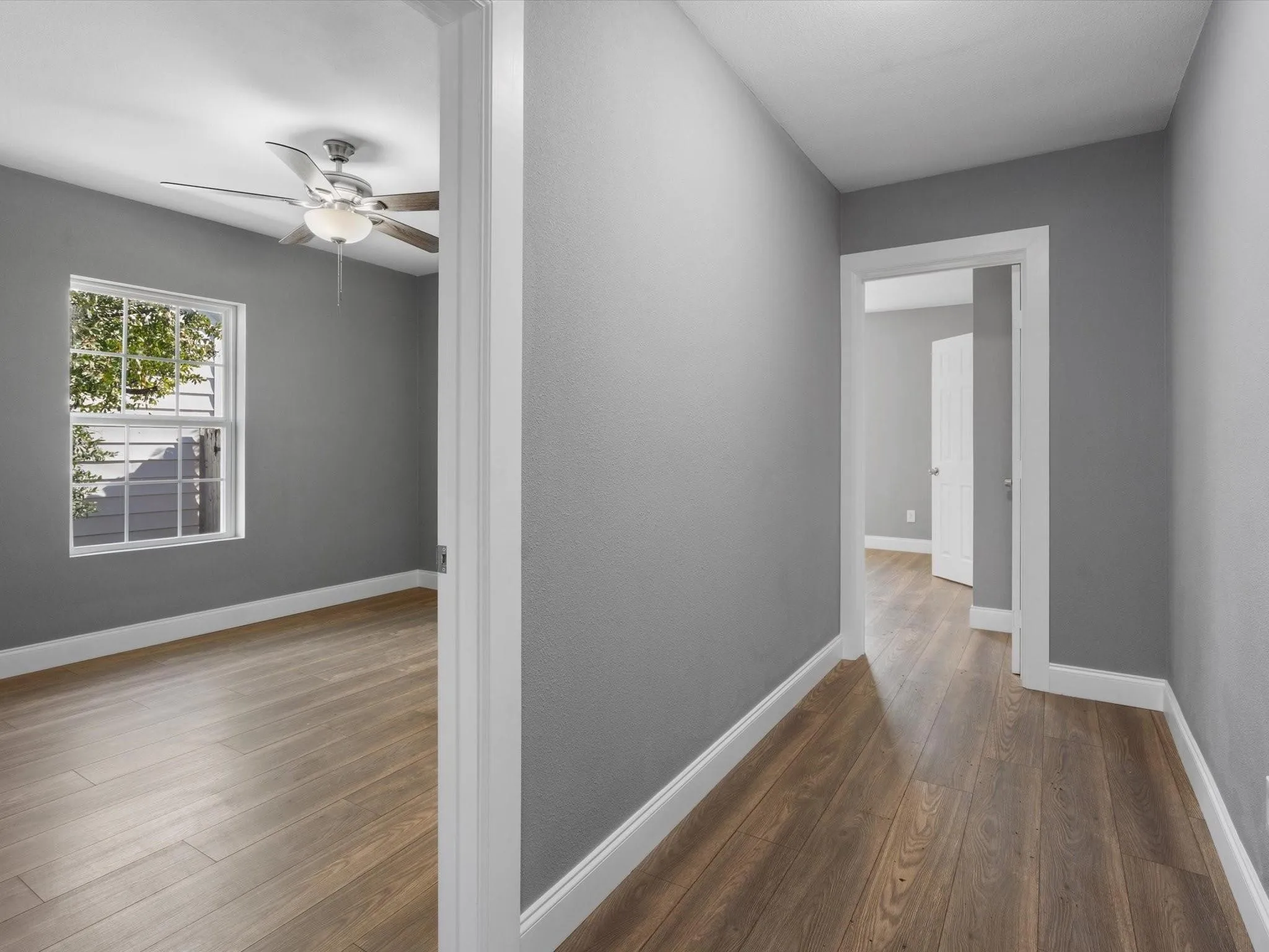 Room with wood-finish flooring, a ceiling fan with integrated lighting, and a white-framed window