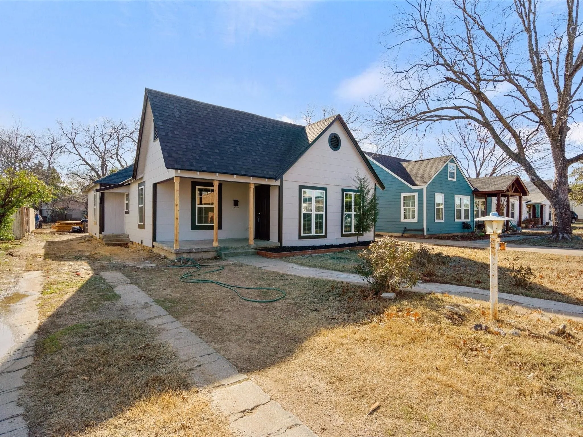 Gabled roofline with dark shingles, light-colored siding, covered front porch with wood columns, white-framed windows, and a paved walkway