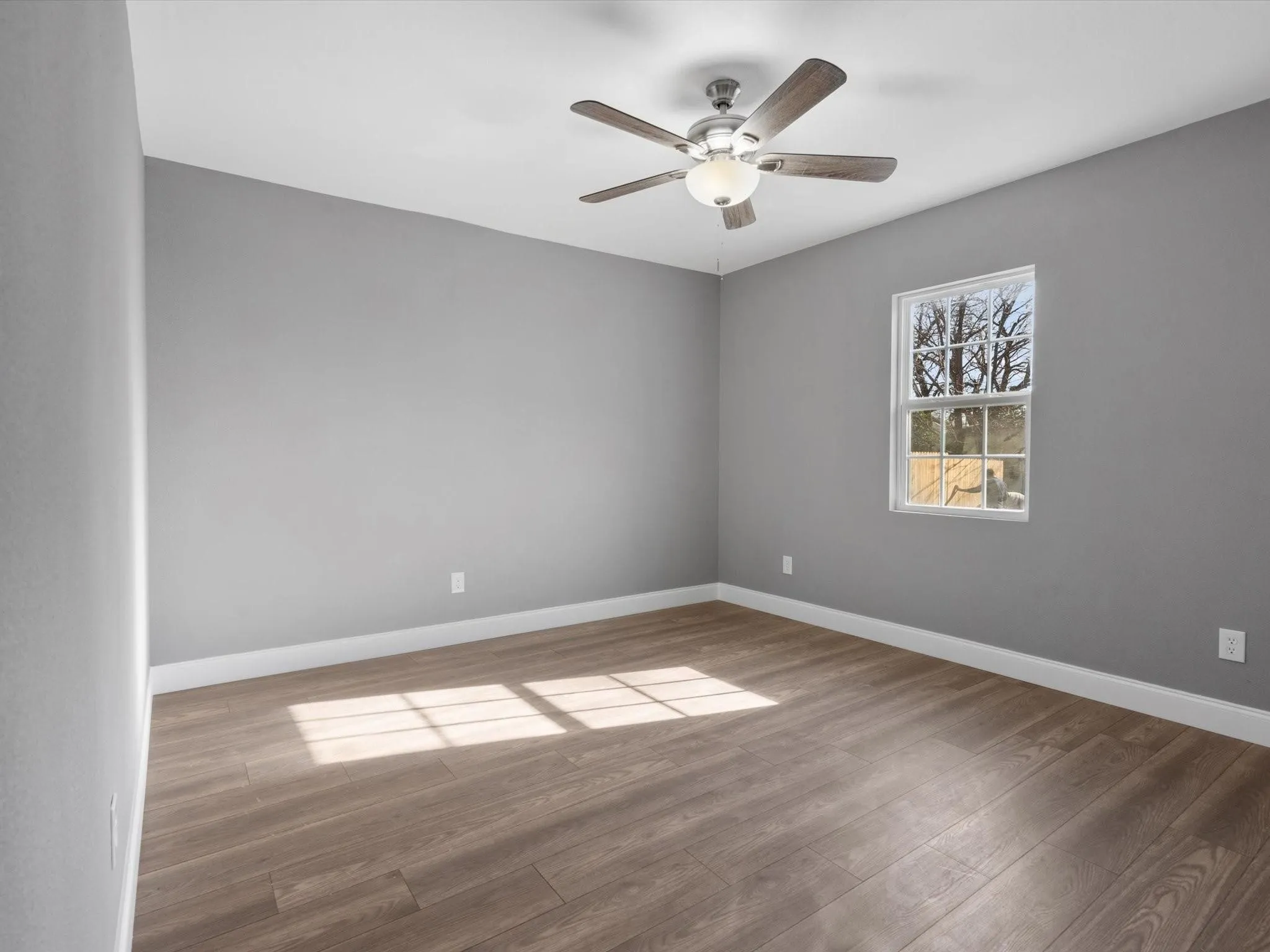 Wood-finish flooring, neutral gray walls, bright white trim, and a ceiling fan with integrated lighting