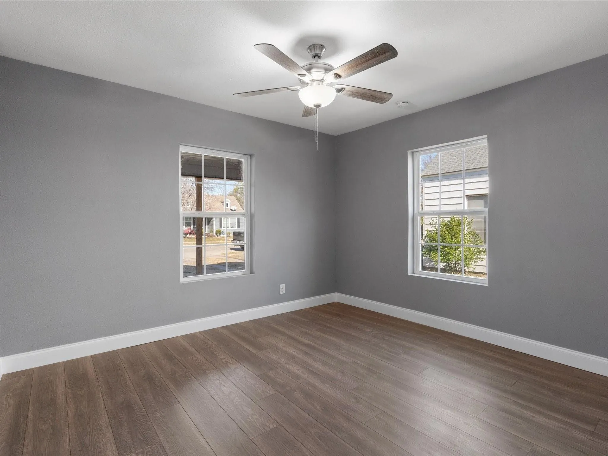 Two double-hung windows with white trim, wood-finish flooring, and a ceiling fan with integrated lighting