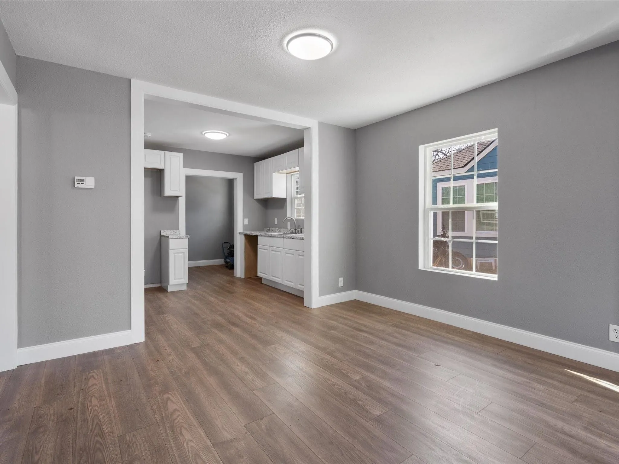 Wood-finish flooring throughout, bright white trim, and a kitchen with white cabinetry and light-toned countertops