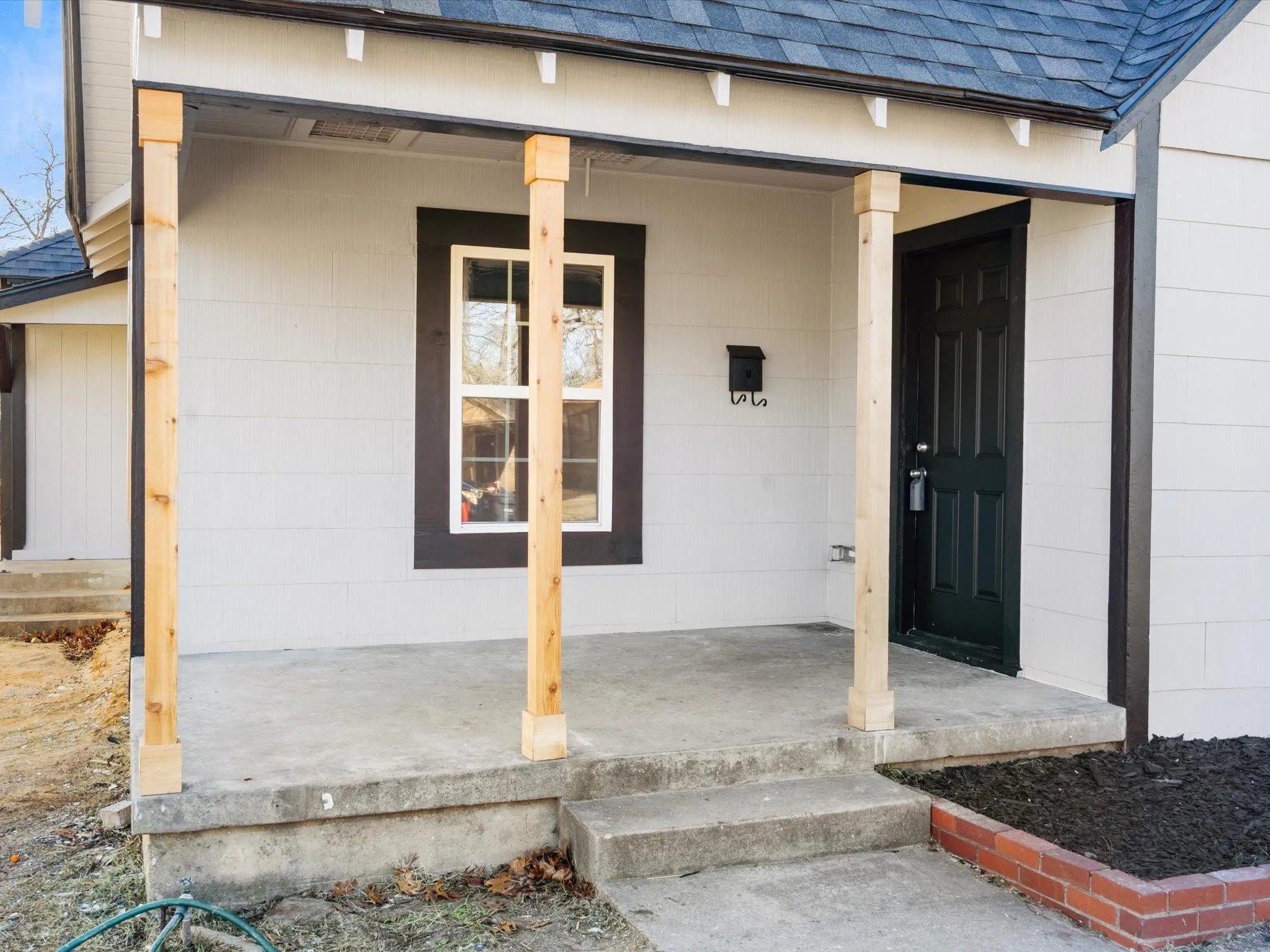 Front porch with concrete steps, wood posts, a dark entry door, and white siding