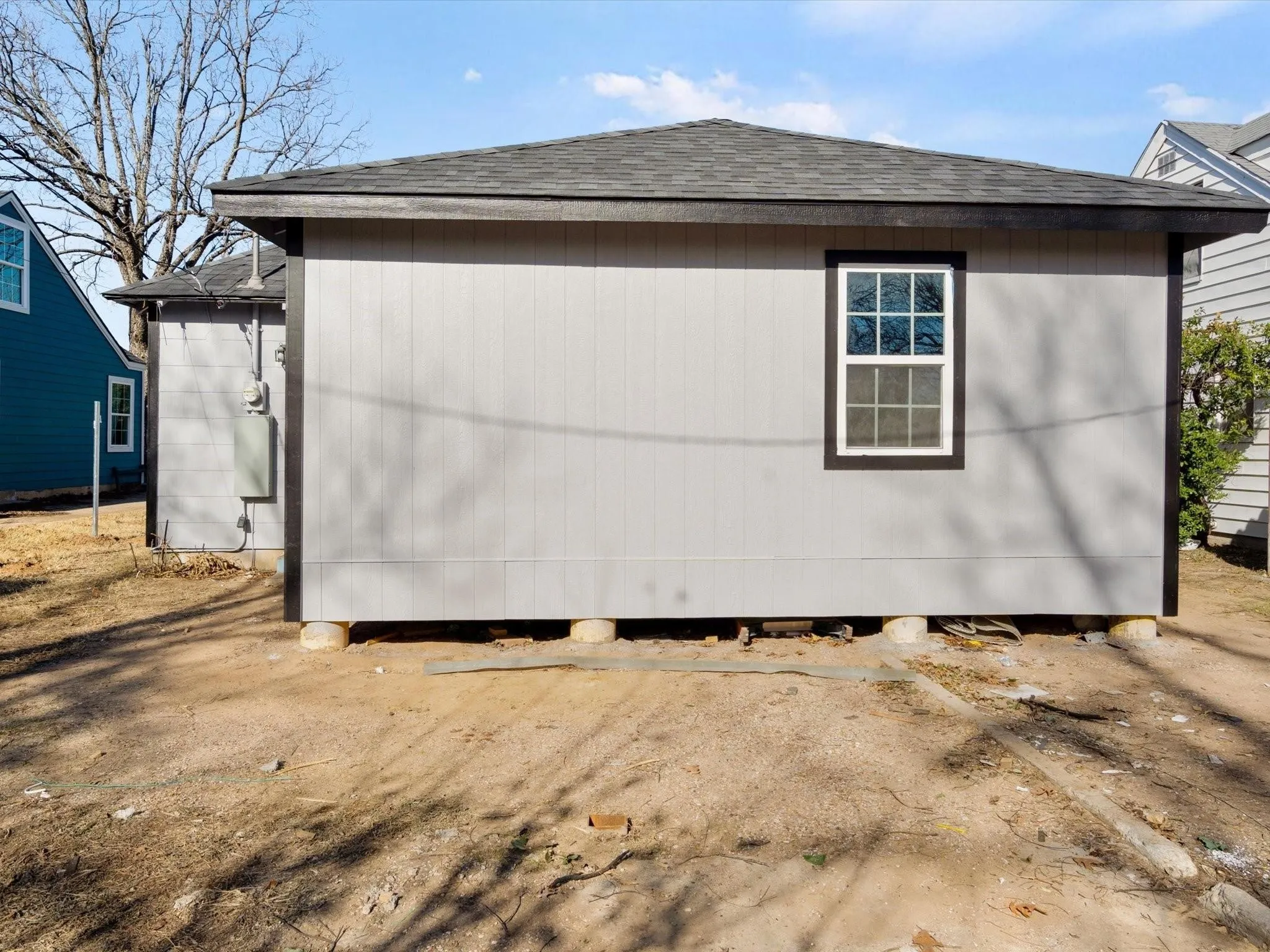 Gray vertical siding exterior with a dark trim window frame and a dark shingle roof