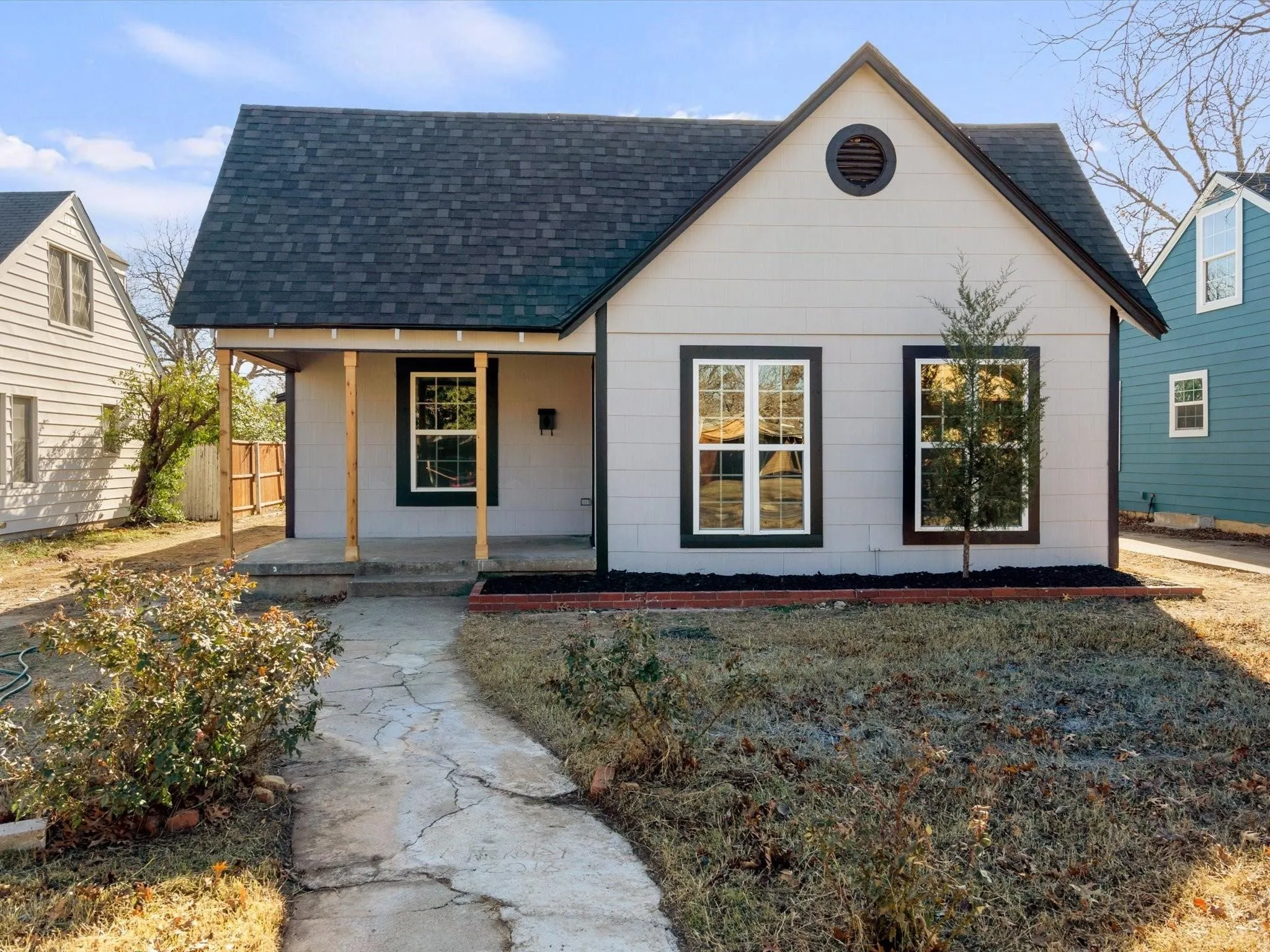 Light gray exterior siding with dark trim windows, dark shingle roof, and a covered porch entry