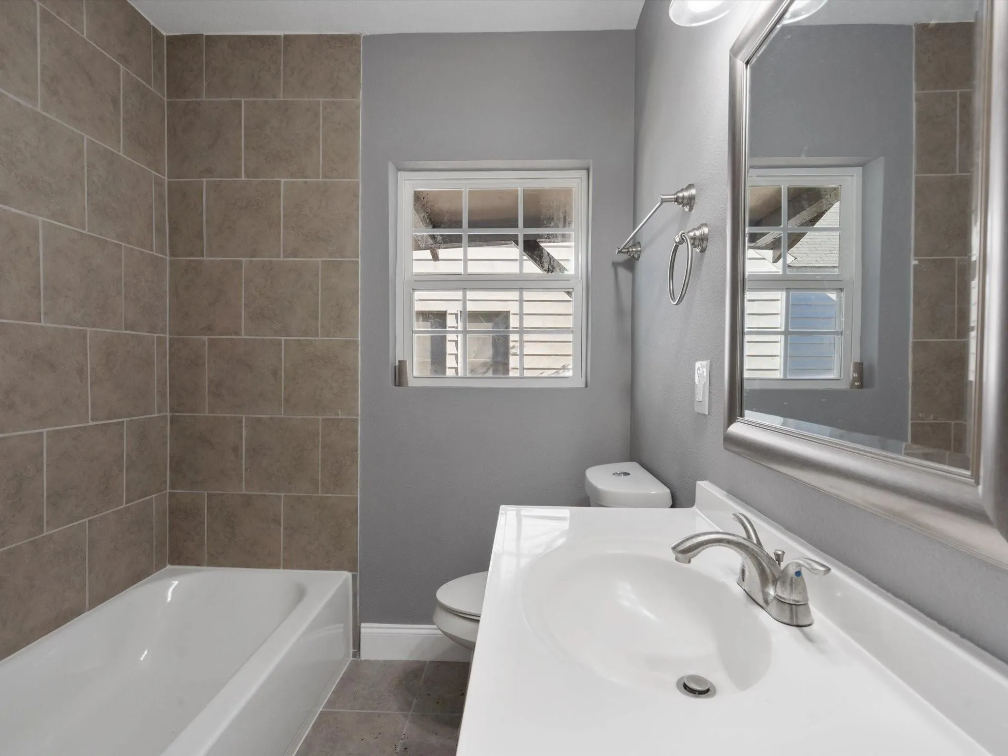 Full bathroom featuring a single vanity with an integrated sink, a large framed mirror, and a window