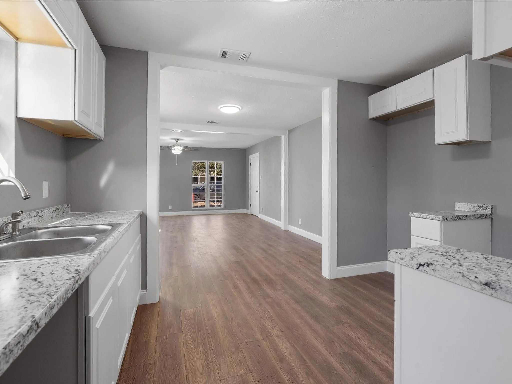 White shaker cabinetry, dual basin stainless steel sink, light-toned countertops, wood-finish flooring, and recessed lighting