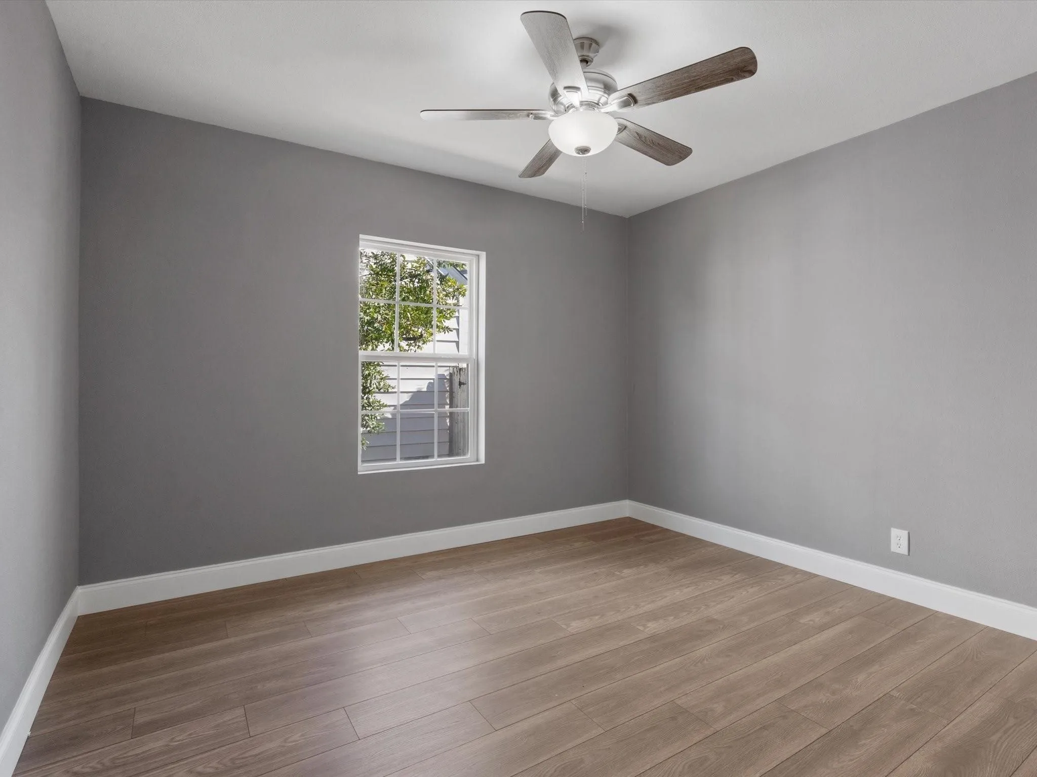 Wood-finish flooring, single window with white trim, ceiling fan, and grey painted walls