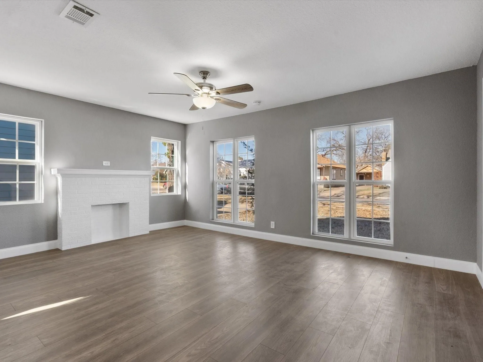 Spacious room featuring wood-finish flooring, multiple windows, a white tile fireplace, and a ceiling fan with integrated lighting