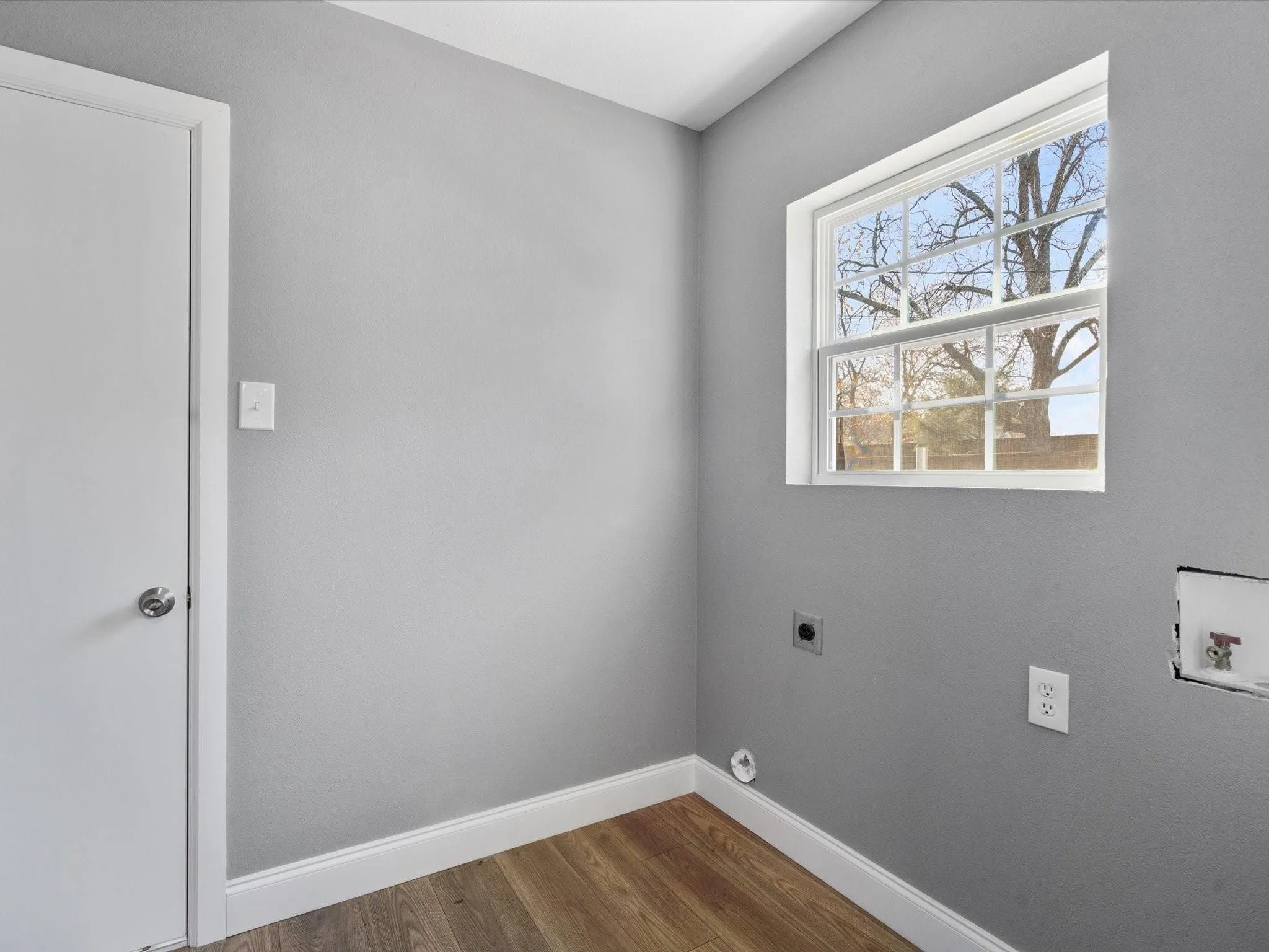 Neutral gray wall finish, wood-finish flooring, white window frame, and laundry hookups