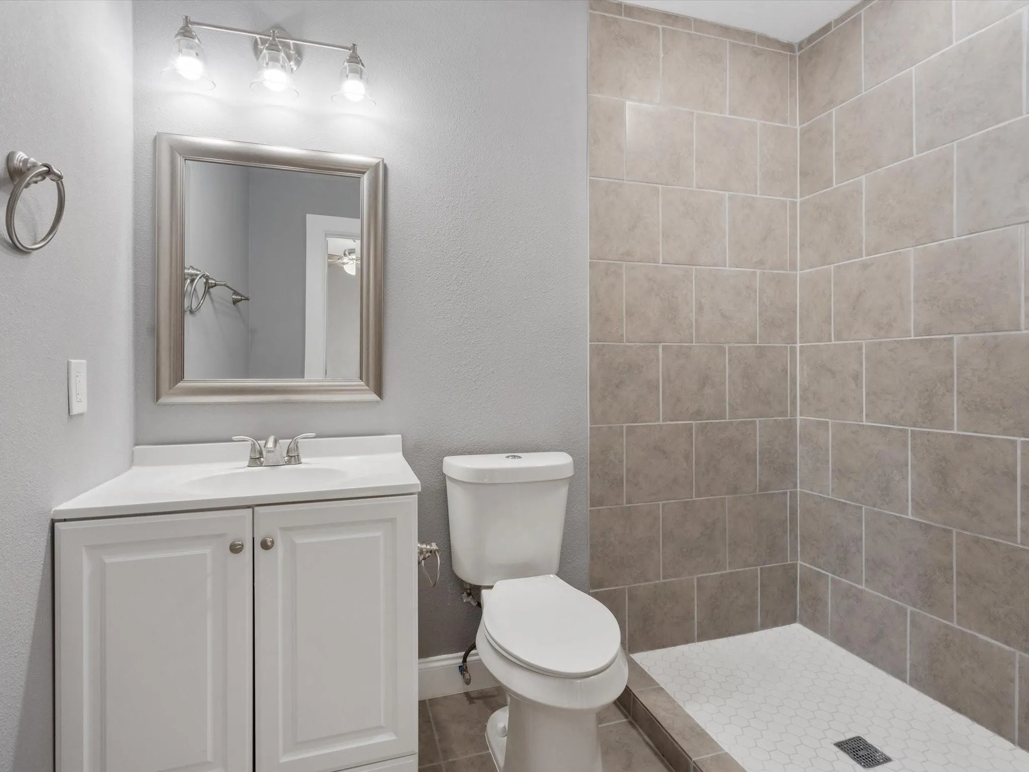 White vanity with shaker-style cabinetry, chrome faucet, framed mirror, and three-light vanity fixture