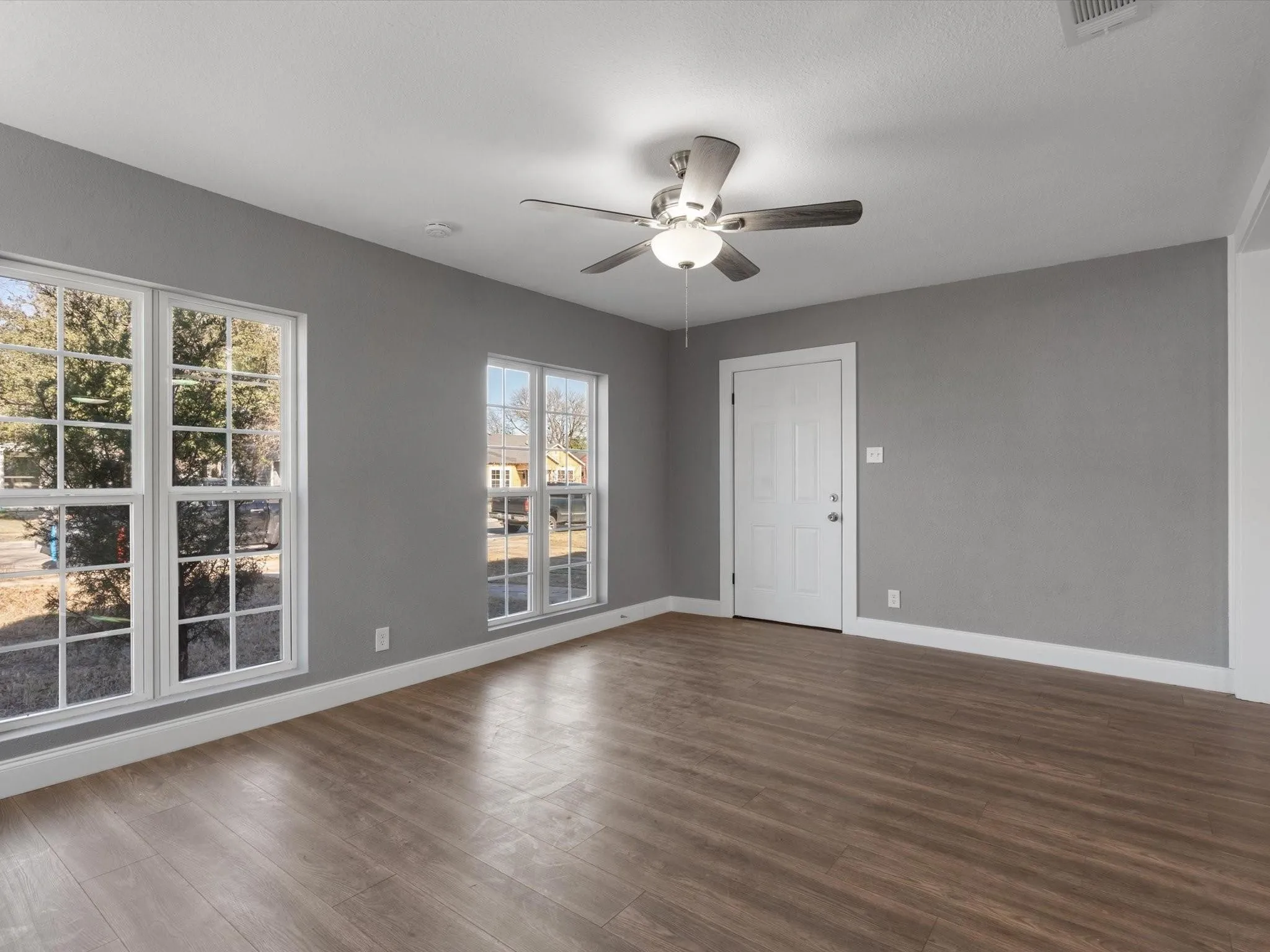 Wood-finish flooring, neutral gray wall tones, white trim, multiple paneled windows, and a ceiling fan with integrated lighting