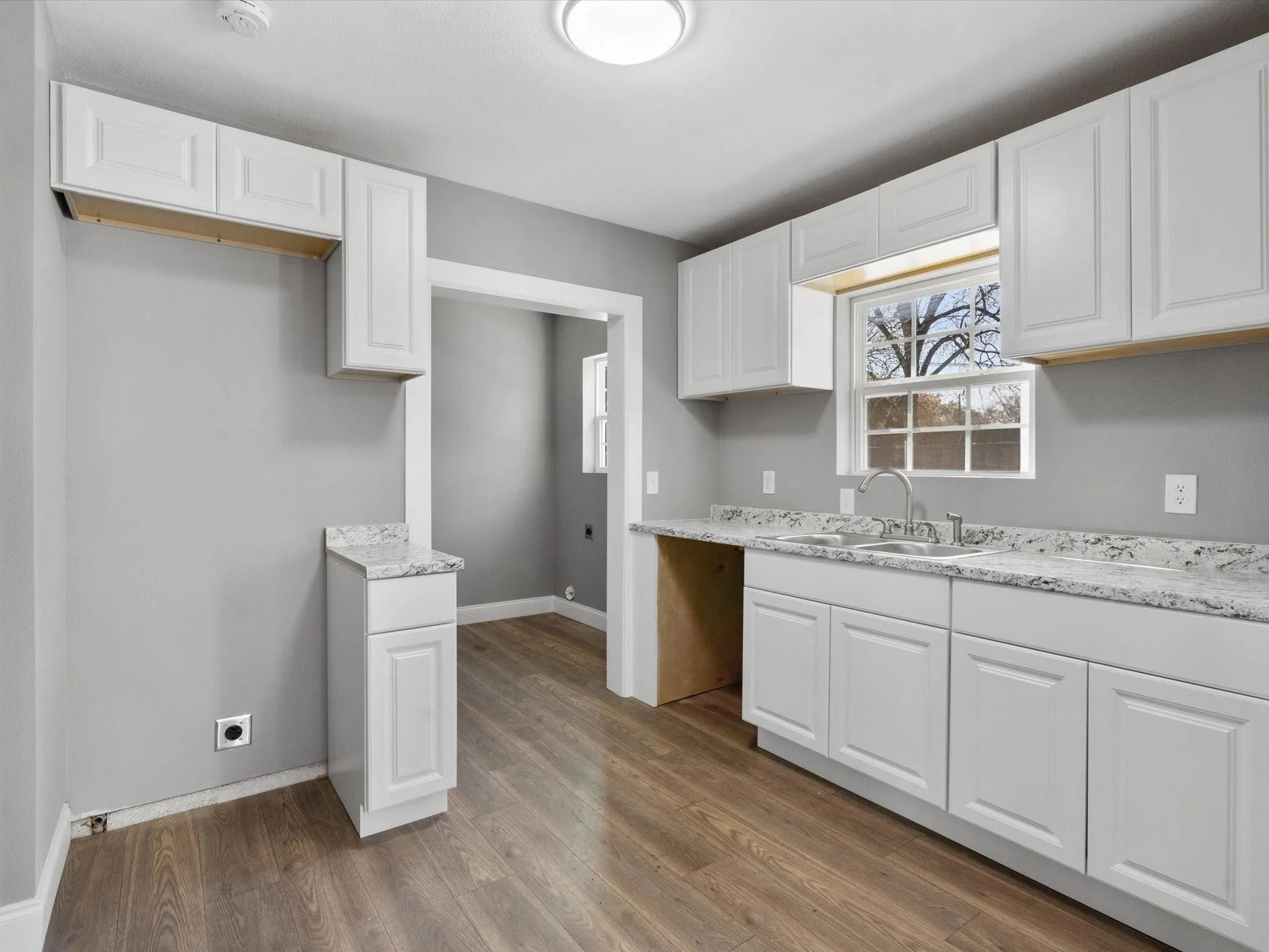 Kitchen featuring white shaker-style cabinetry, wood-finish flooring, light-toned countertops, and a stainless steel sink with a gooseneck faucet
