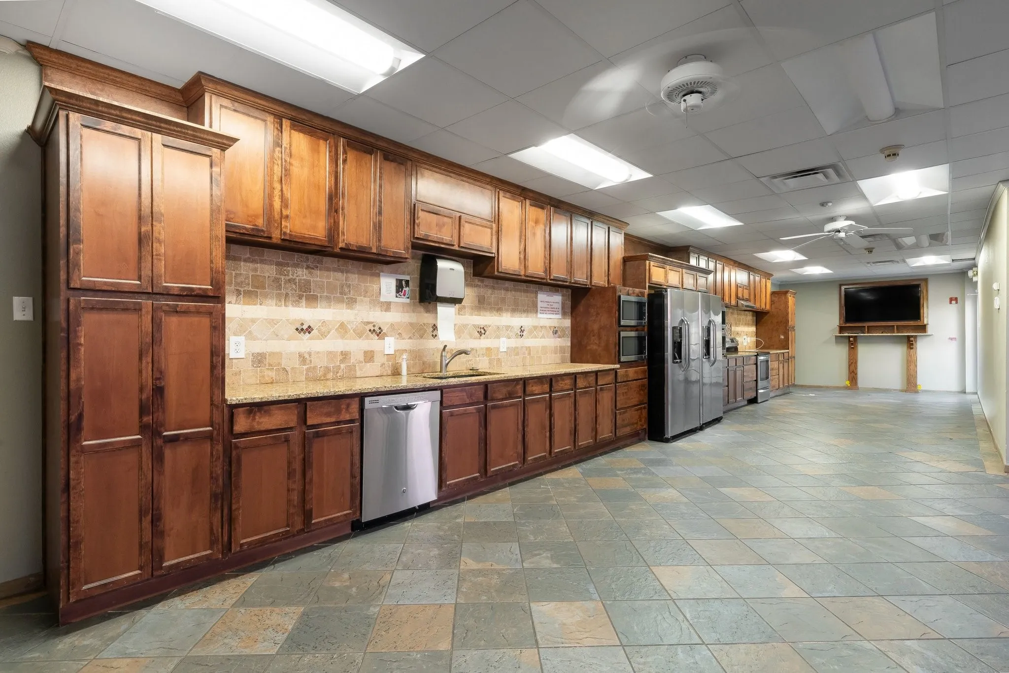Expansive kitchen space featuring abundant wood cabinetry, integrated stainless steel appliances, granite countertops, a tiled backsplash, and durable tile flooring