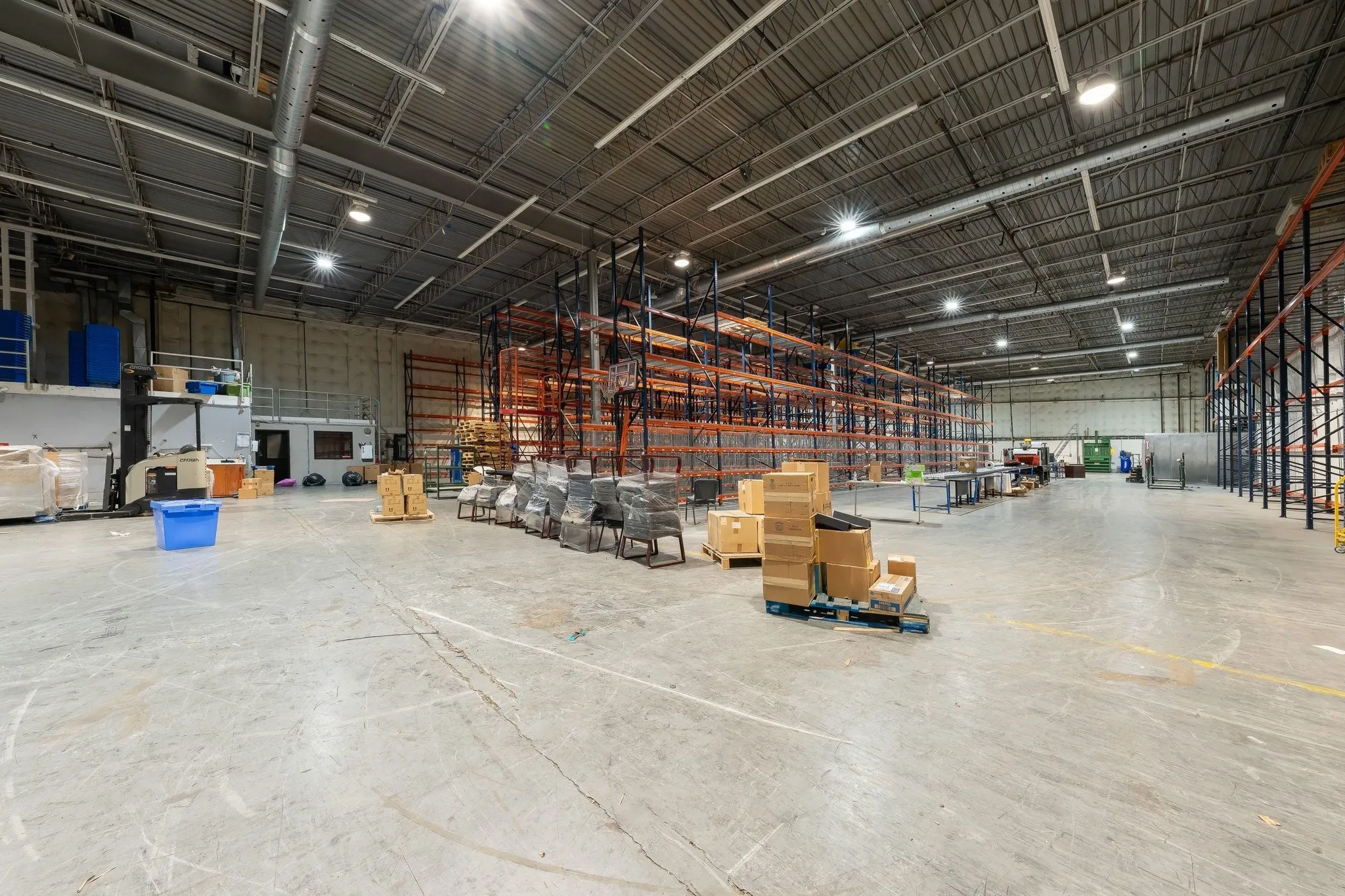 Spacious industrial facility with a concrete floor, high ceilings, exposed ductwork, and fluorescent lighting
