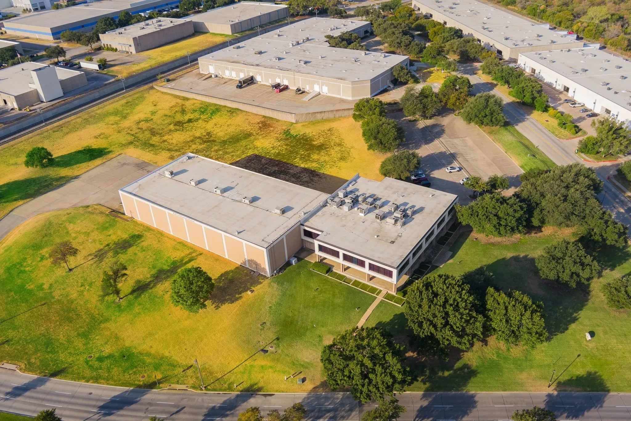 Industrial building with a tan facade, multiple windows, and extensive surrounding green space