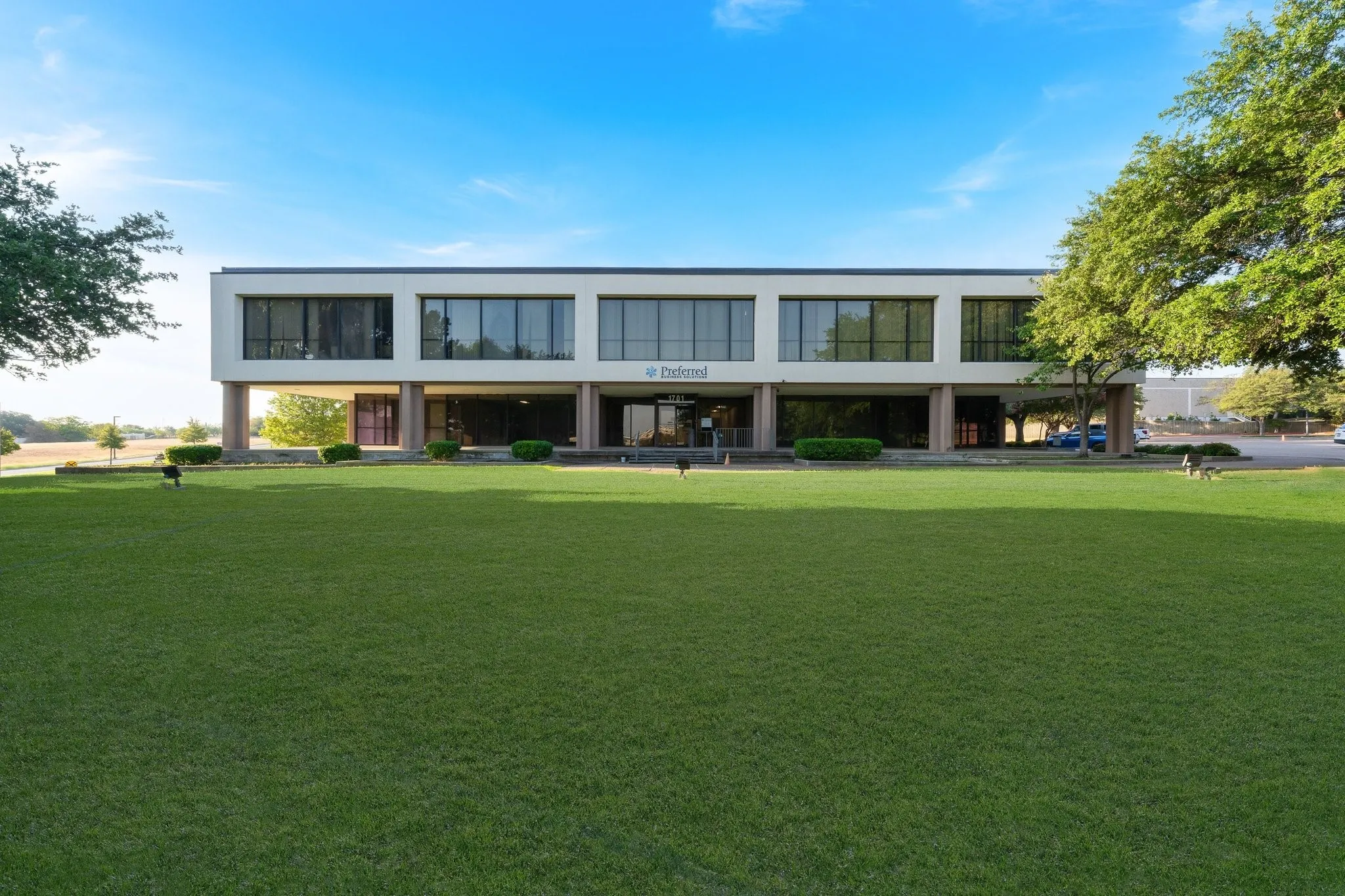 Two-story commercial building featuring extensive landscaping, columned entrance, and large windows