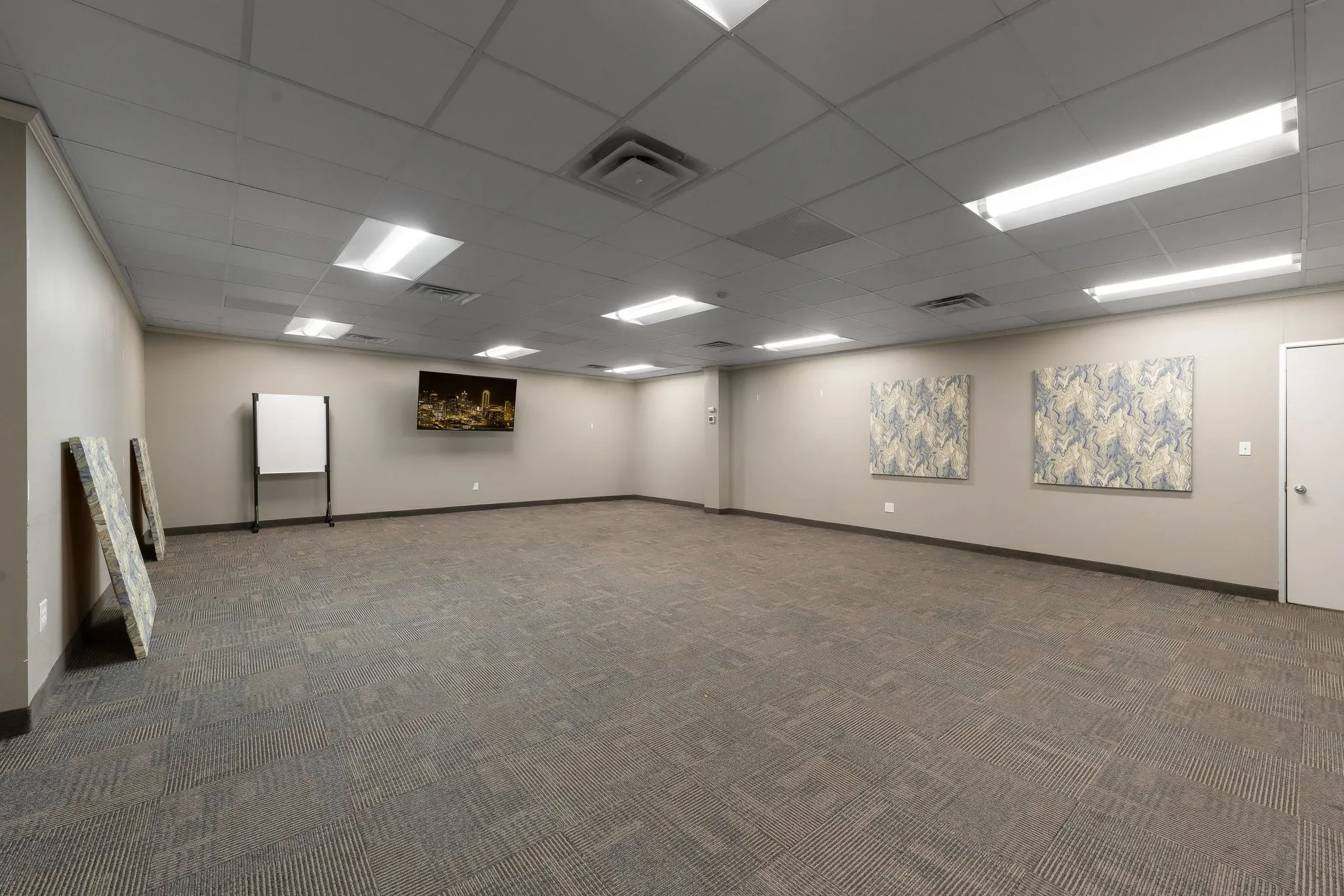Recessed ceiling panels, ample overhead lighting, neutral wall tones, and patterned carpet flooring, conference room or training space.