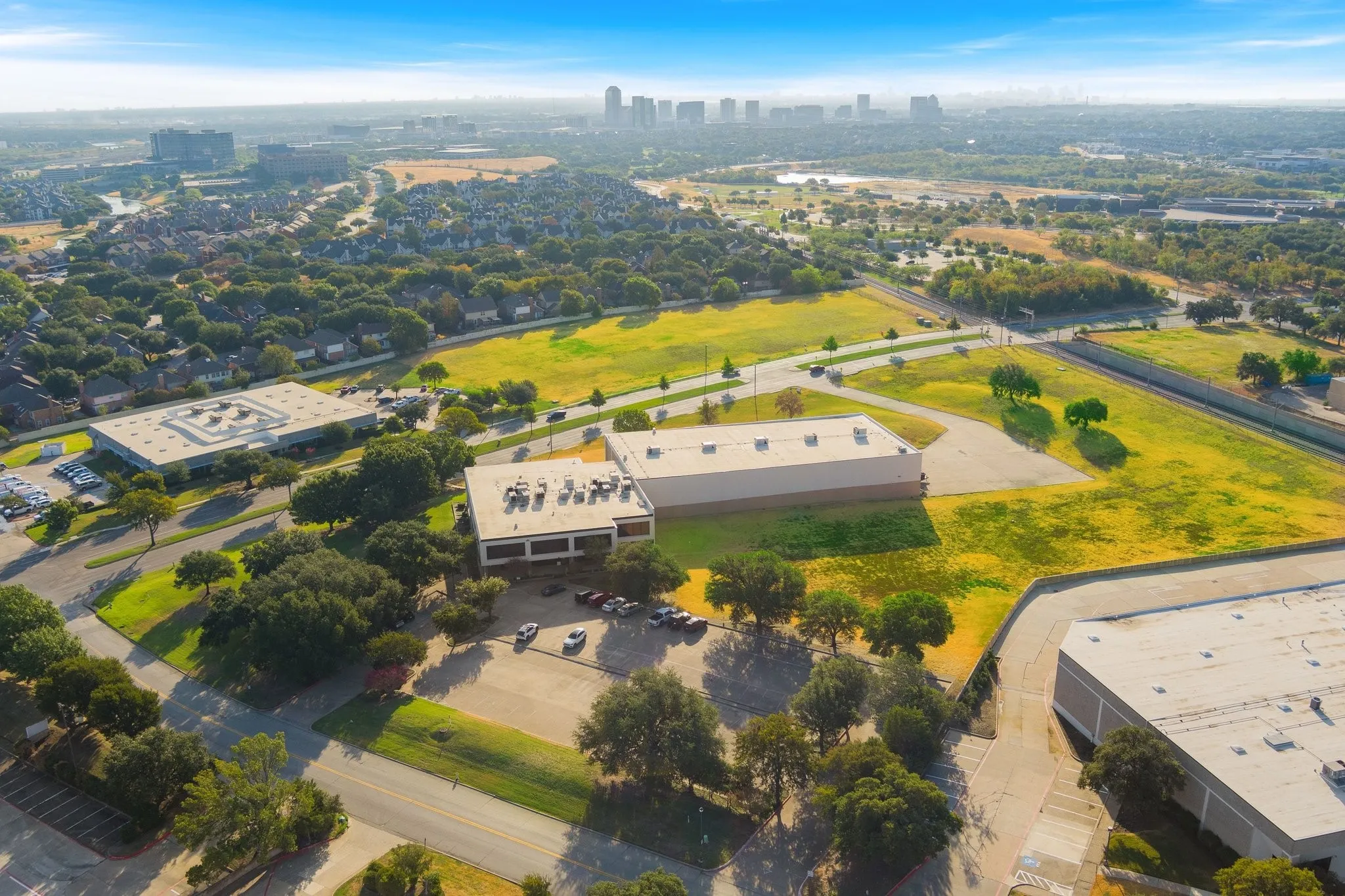 Aerial perspective showcasing multiple commercial buildings, extensive open land, and surrounding mature trees
