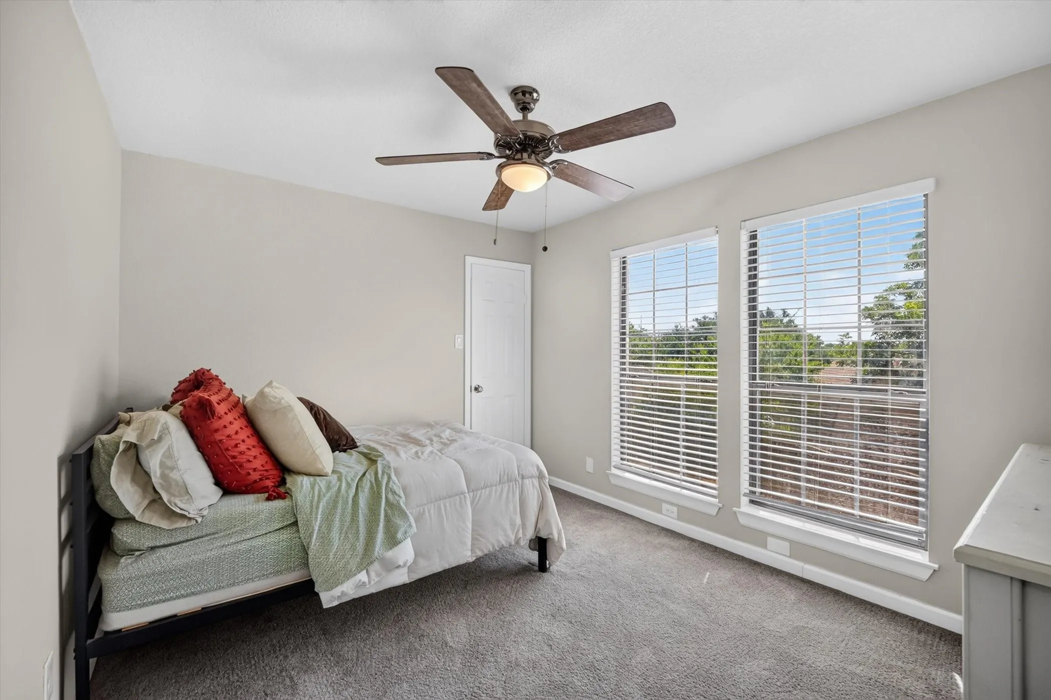 Carpeted room with a ceiling fan, two windows with blinds, and white trim