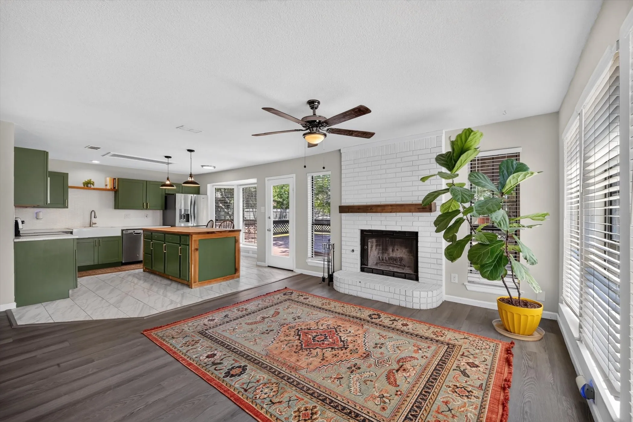 Open-concept living space featuring a white brick fireplace with a wood-finish mantel, dark wood-finish flooring, and a ceiling fan