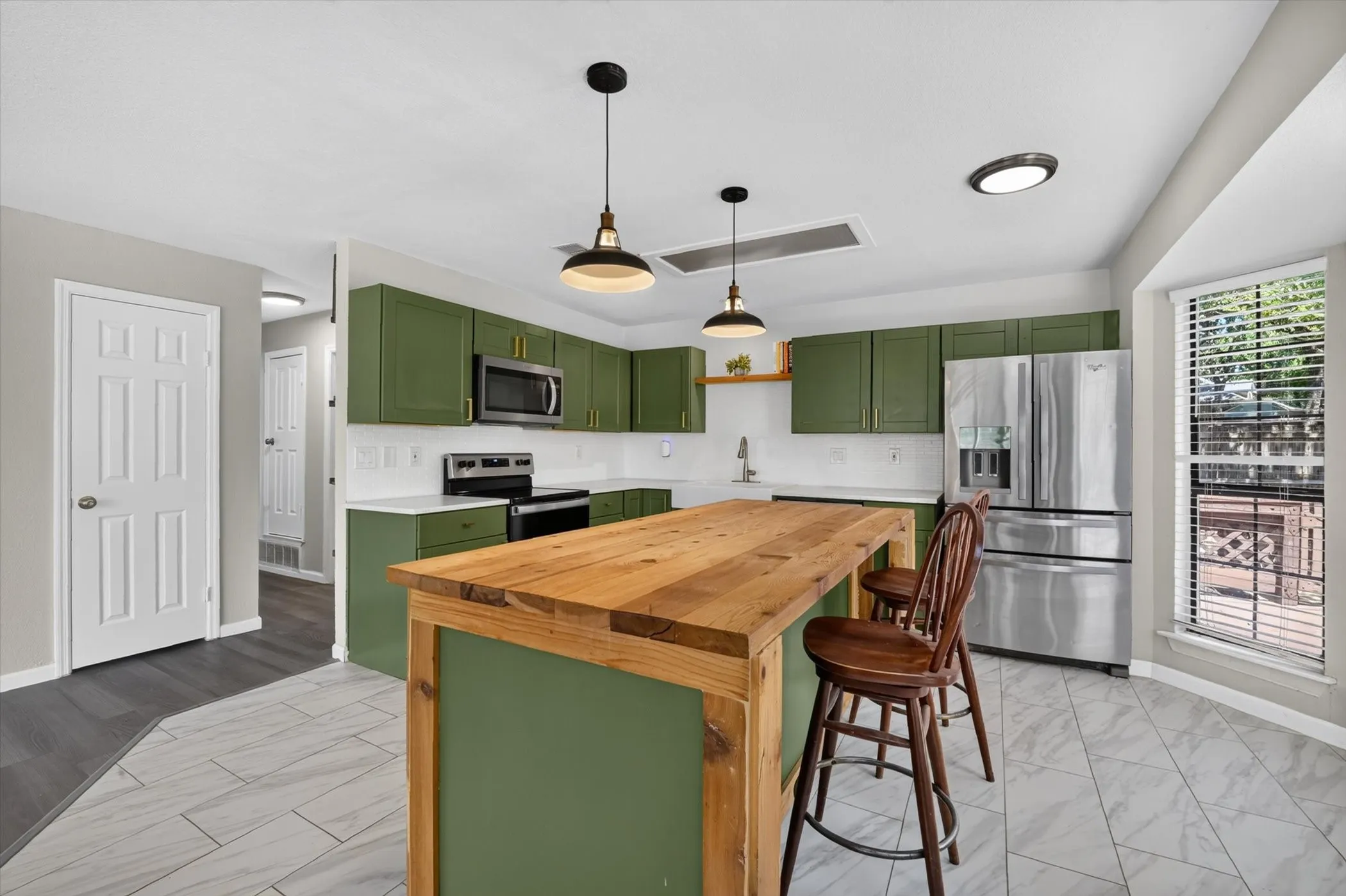 Kitchen featuring green cabinetry, stainless steel appliances, white countertops, and a wood-finish island