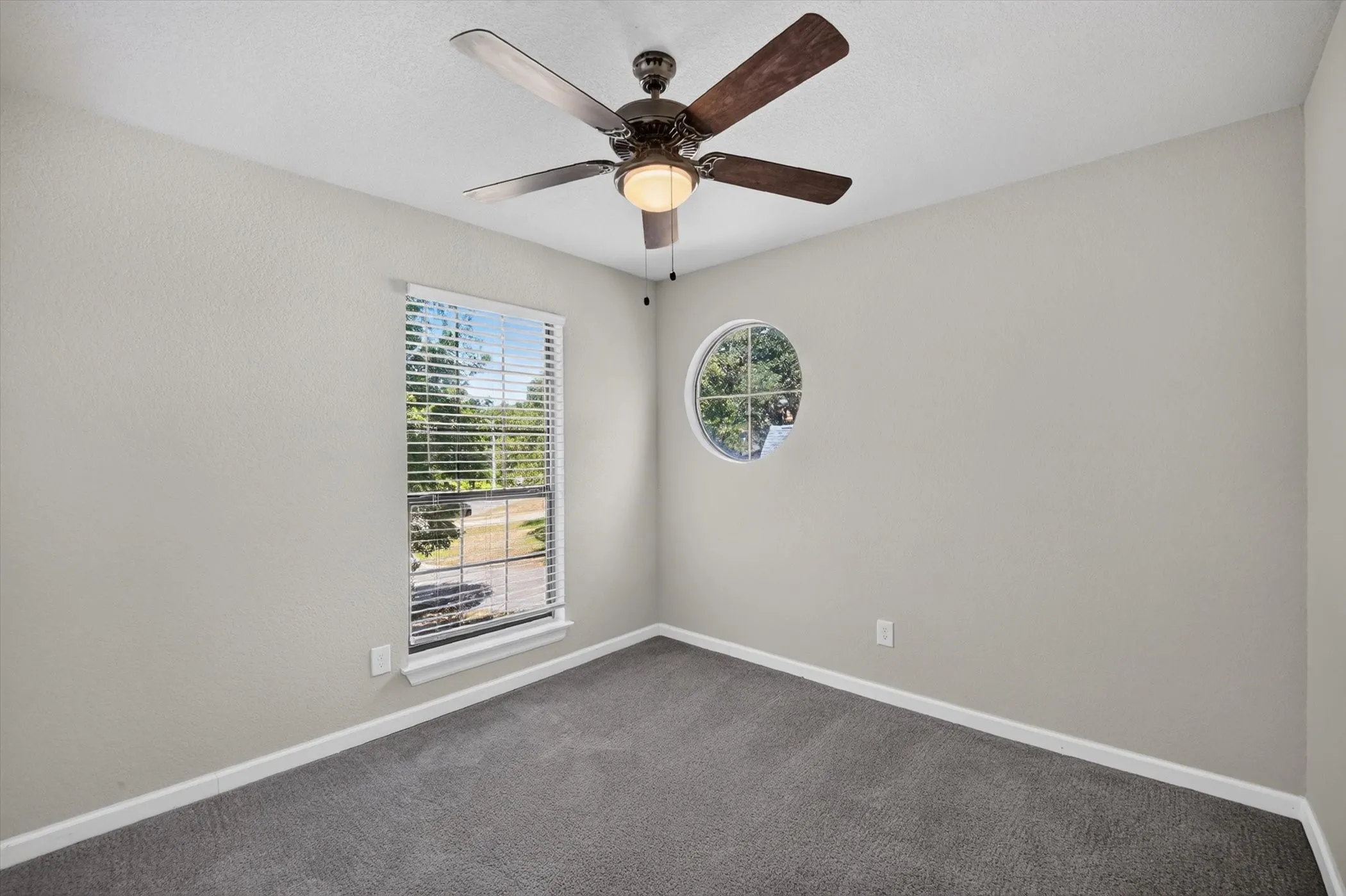 Carpeted room featuring a ceiling fan with light, rectangular window with blinds, and a circular window
