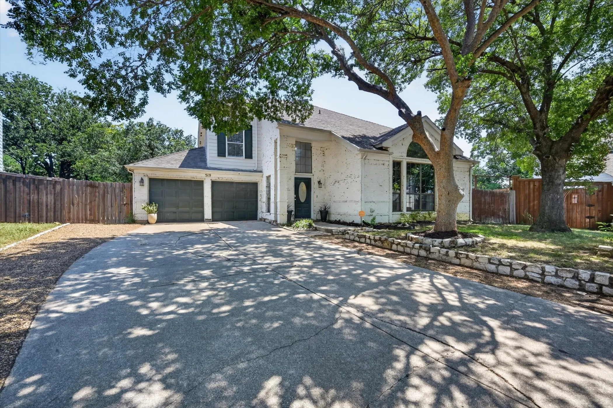 Lime wash brick exterior with a two-car garage, large driveway, arched windows, and a stone retaining wall