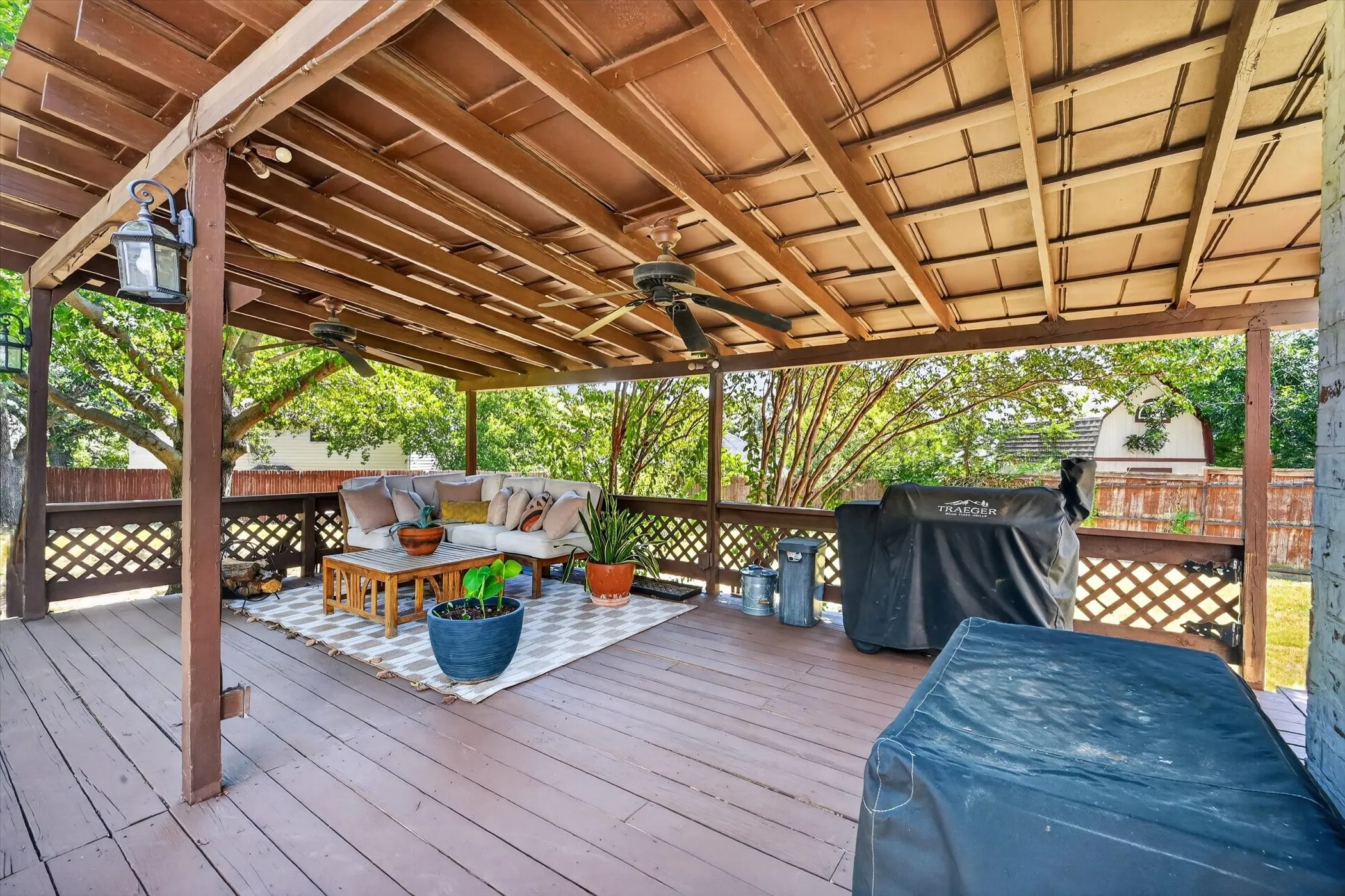 Expansive wood-finish deck with a latticework railing, covered by a wood-beamed patio roof with ceiling fans and pendant lighting