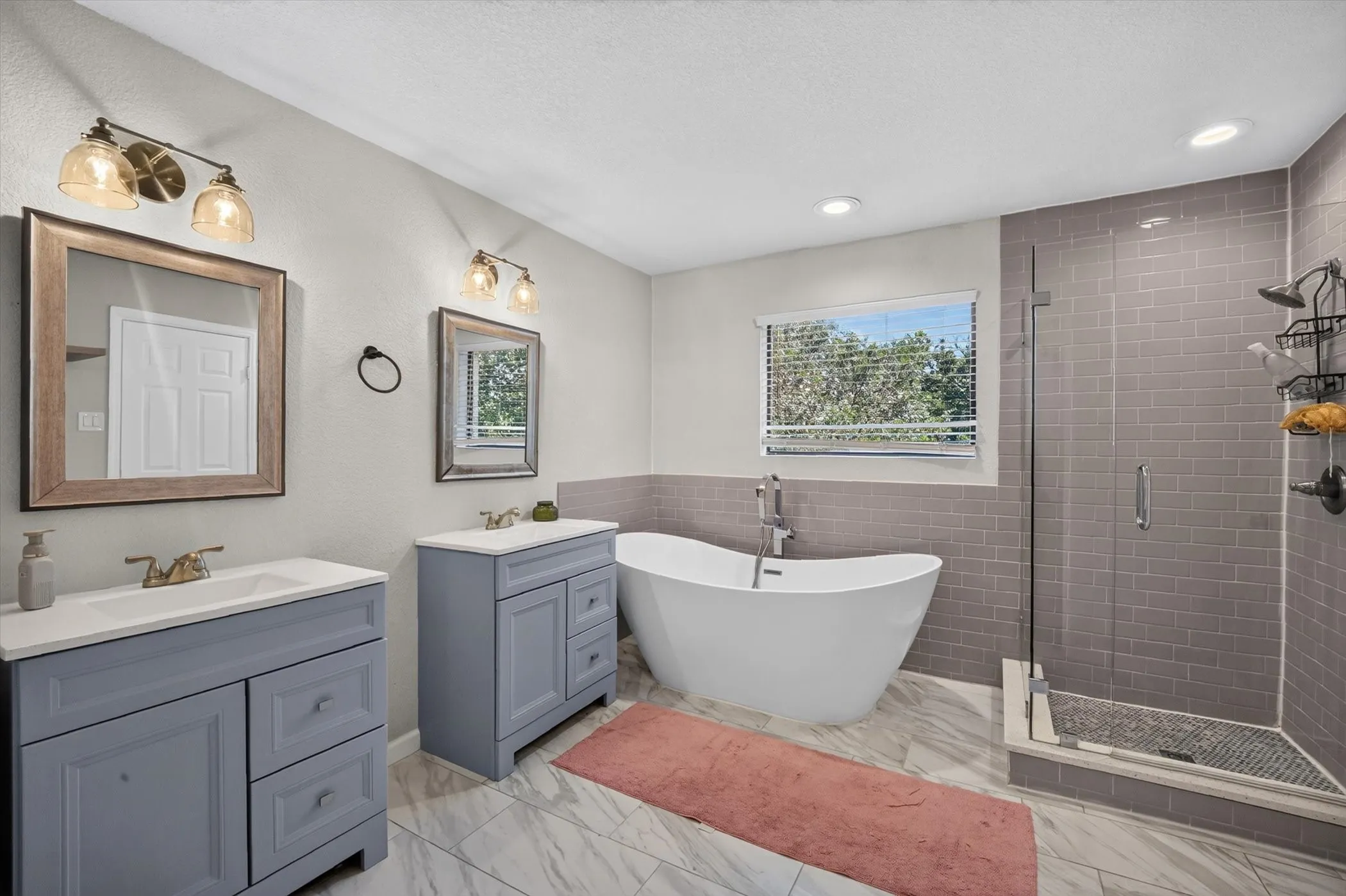 Dual vanities, freestanding soaking tub, glass-enclosed shower with subway tile surround, recessed lighting, and wood-finish flooring