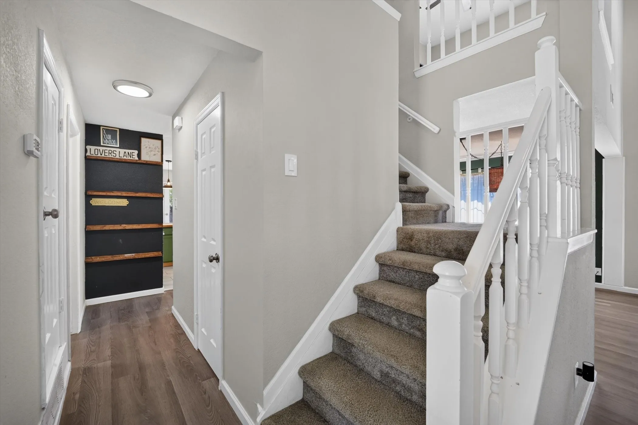 Wood-finish flooring, neutral wall tones, carpeted staircase, white newel posts, and balusters