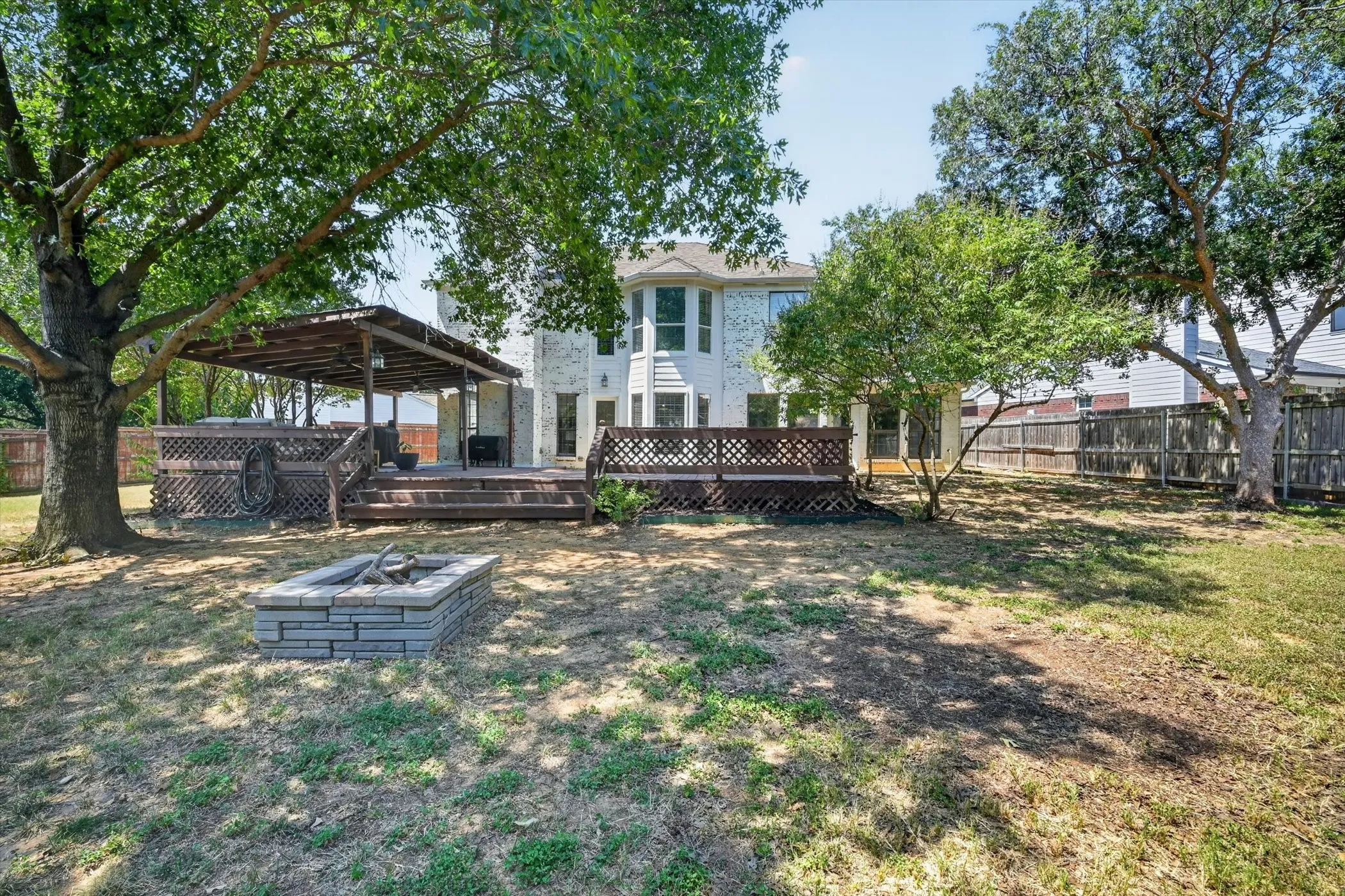 Expansive backyard featuring a multi-level wood deck, a covered patio area, and a built-in stone fire pit