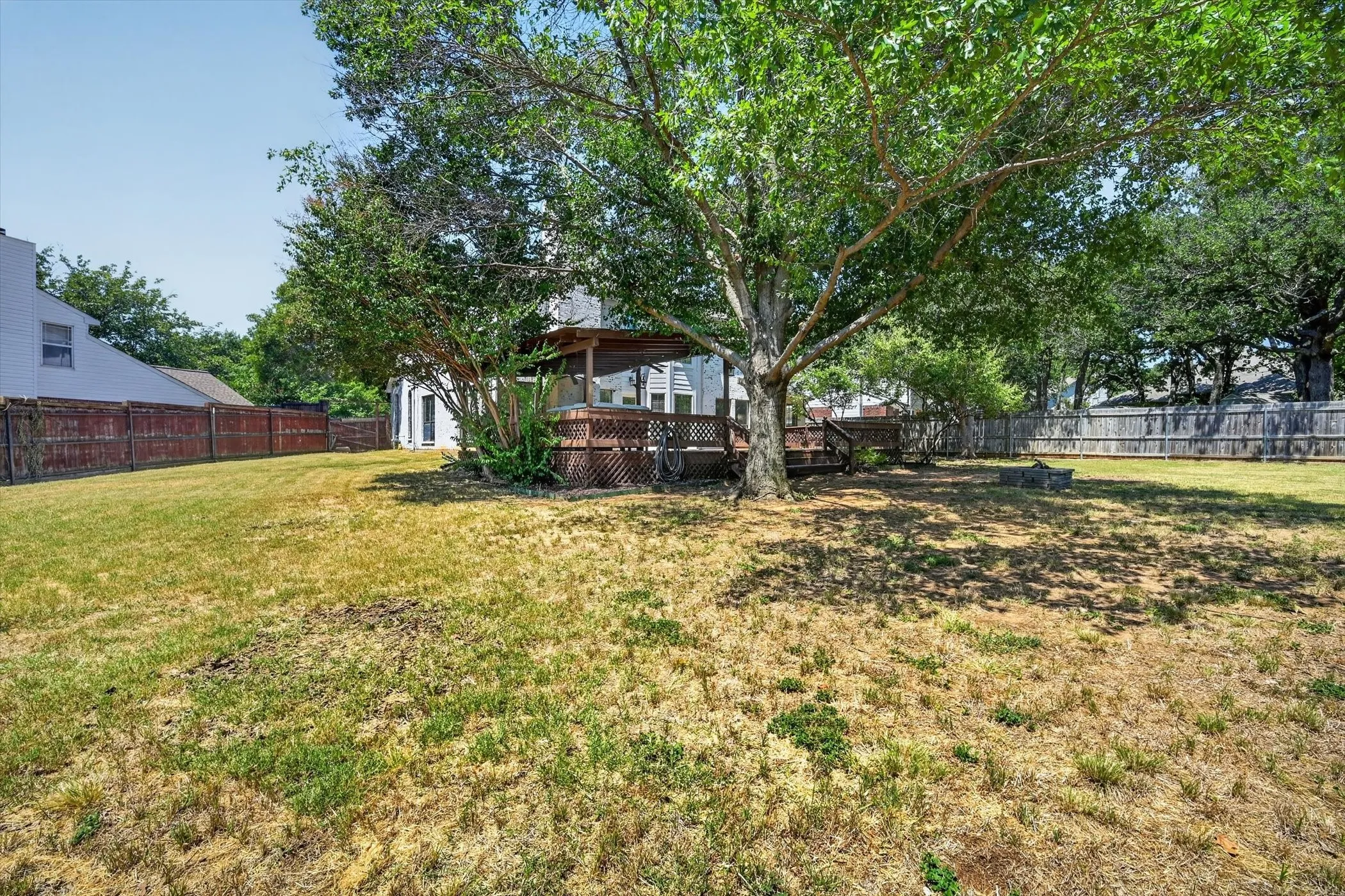 Expansive backyard featuring a mature shade tree, a wood deck with lattice skirting, and a privacy fence