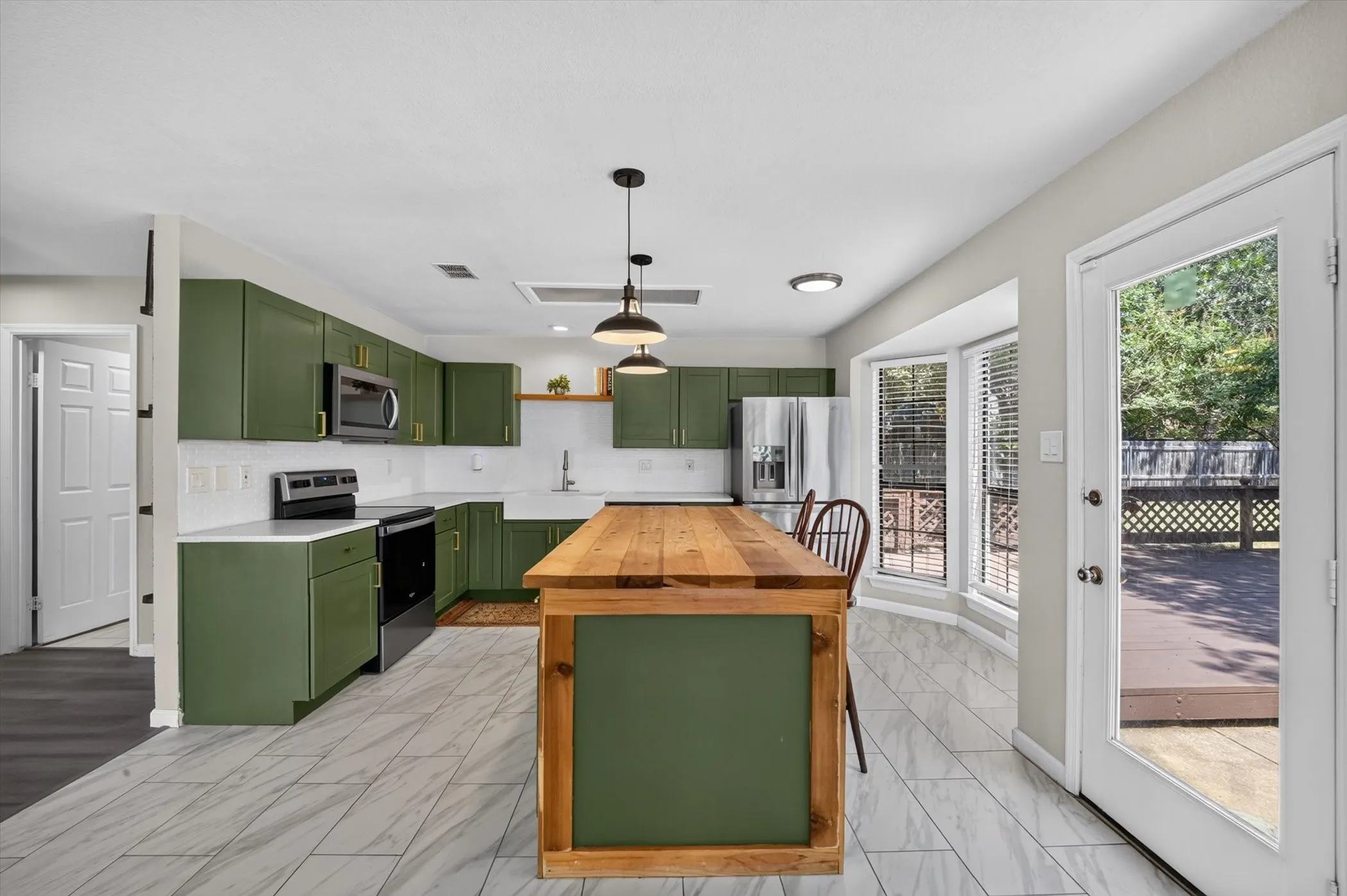 Kitchen featuring green cabinetry, white countertops, tile flooring, a wood-finish island, and a glass-paneled door opening to a deck