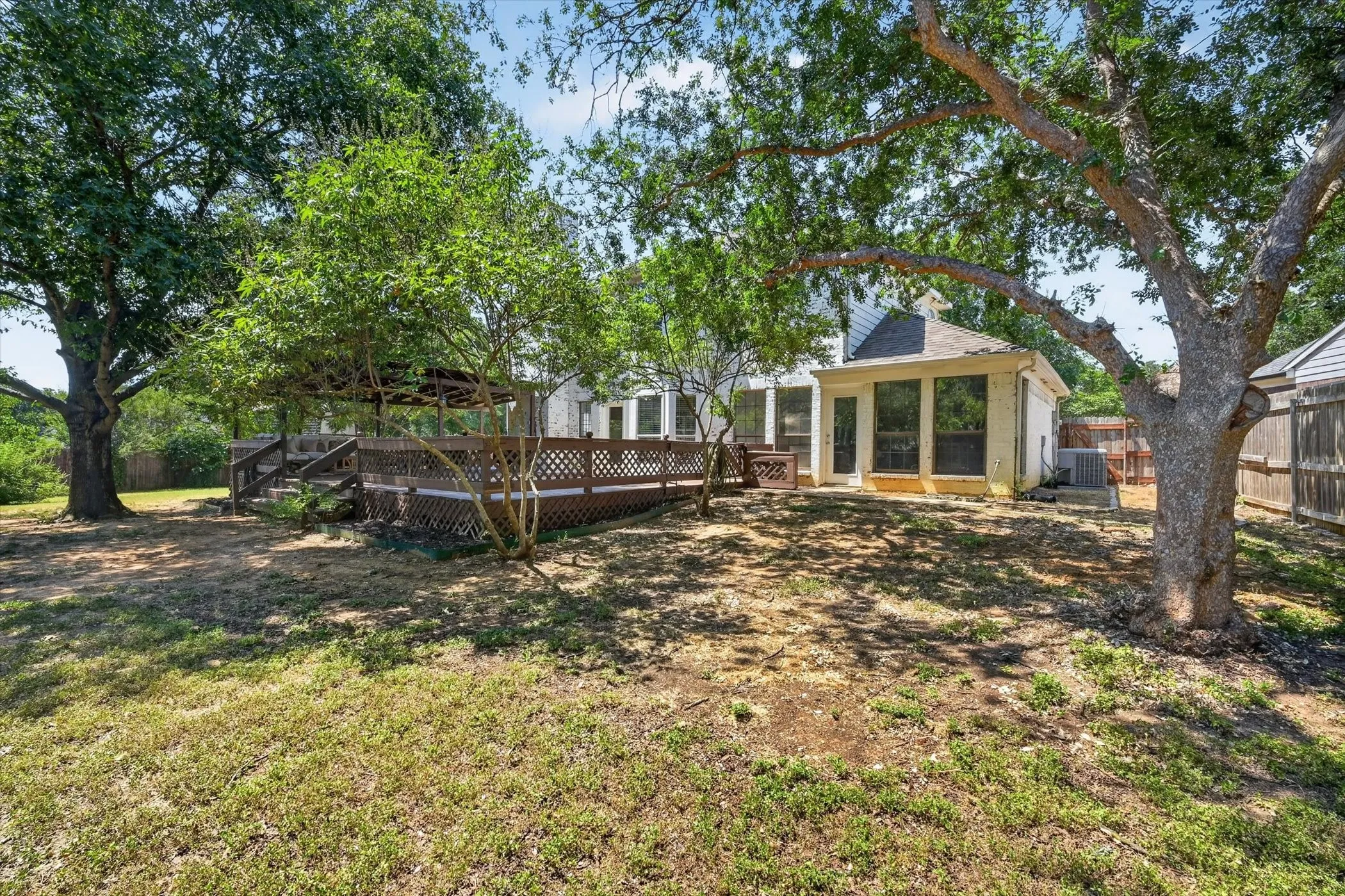 Expansive backyard featuring a multi-level wood deck, mature trees, and a screened-in porch
