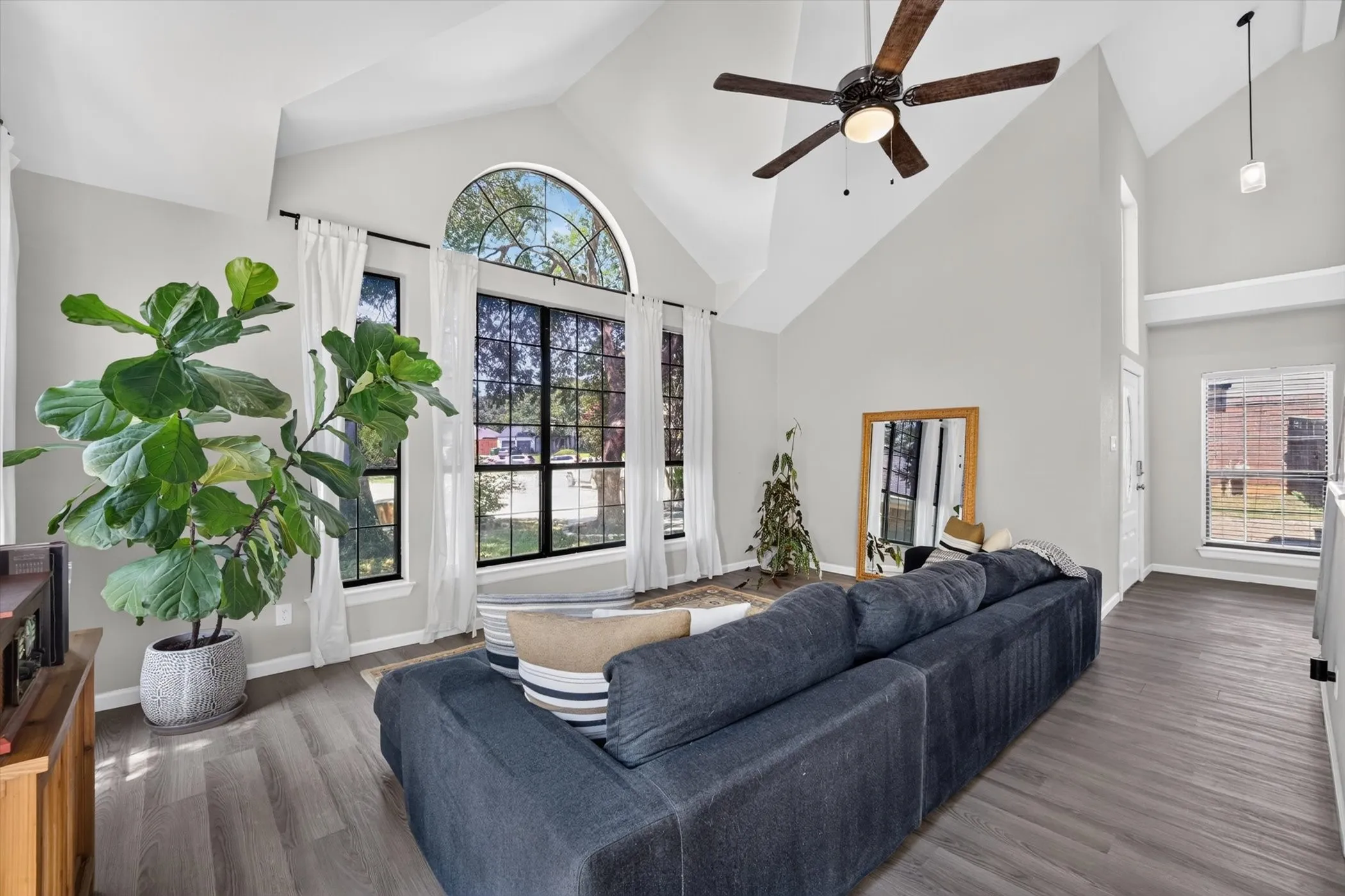 Vaulted ceilings, a dark wood-finish ceiling fan, and large windows with an arched transom