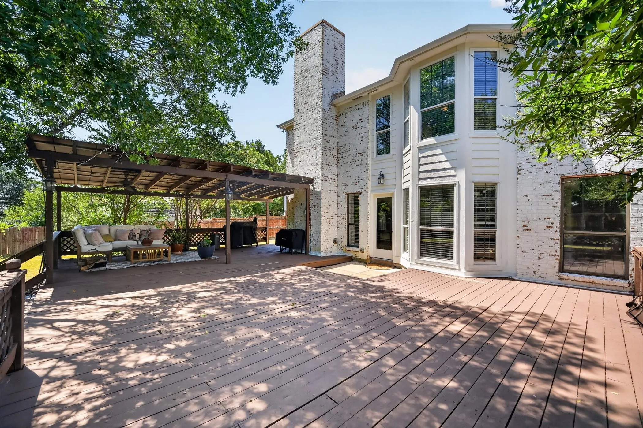 Expansive wood-finish deck with a built-in pergola, offering direct access to the interior through a glass-paneled door