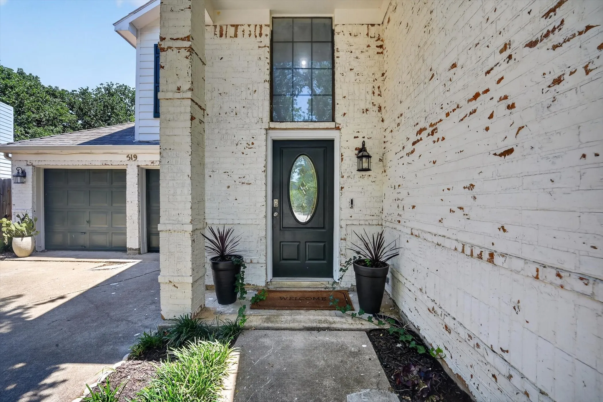Lime wash brick exterior, covered front entry, dark paneled front door with oval glass insert, transom window, and attached lantern-style light fixture