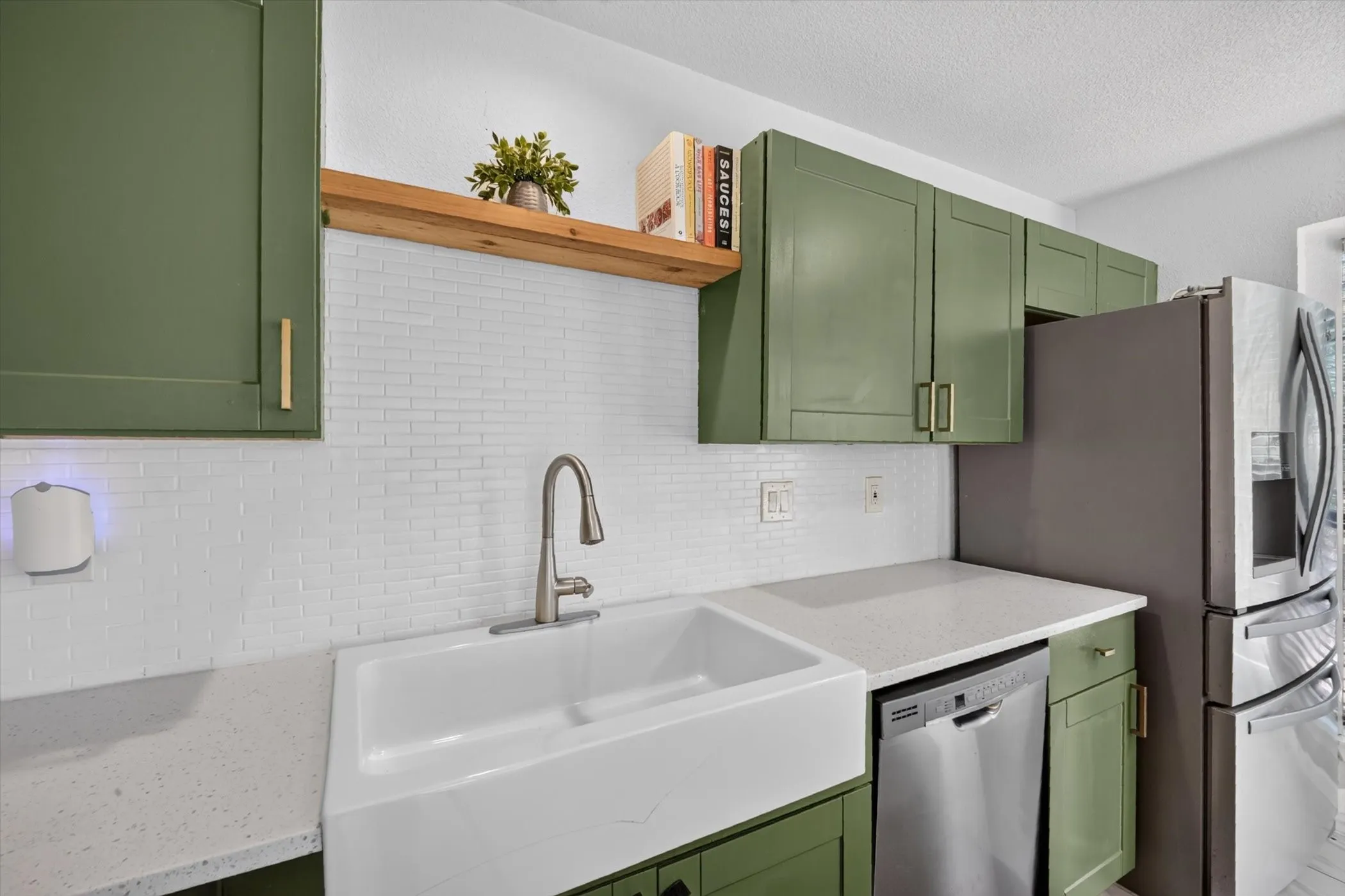 Kitchen featuring green cabinetry, white subway tile backsplash, white farmhouse sink, and light-toned countertops