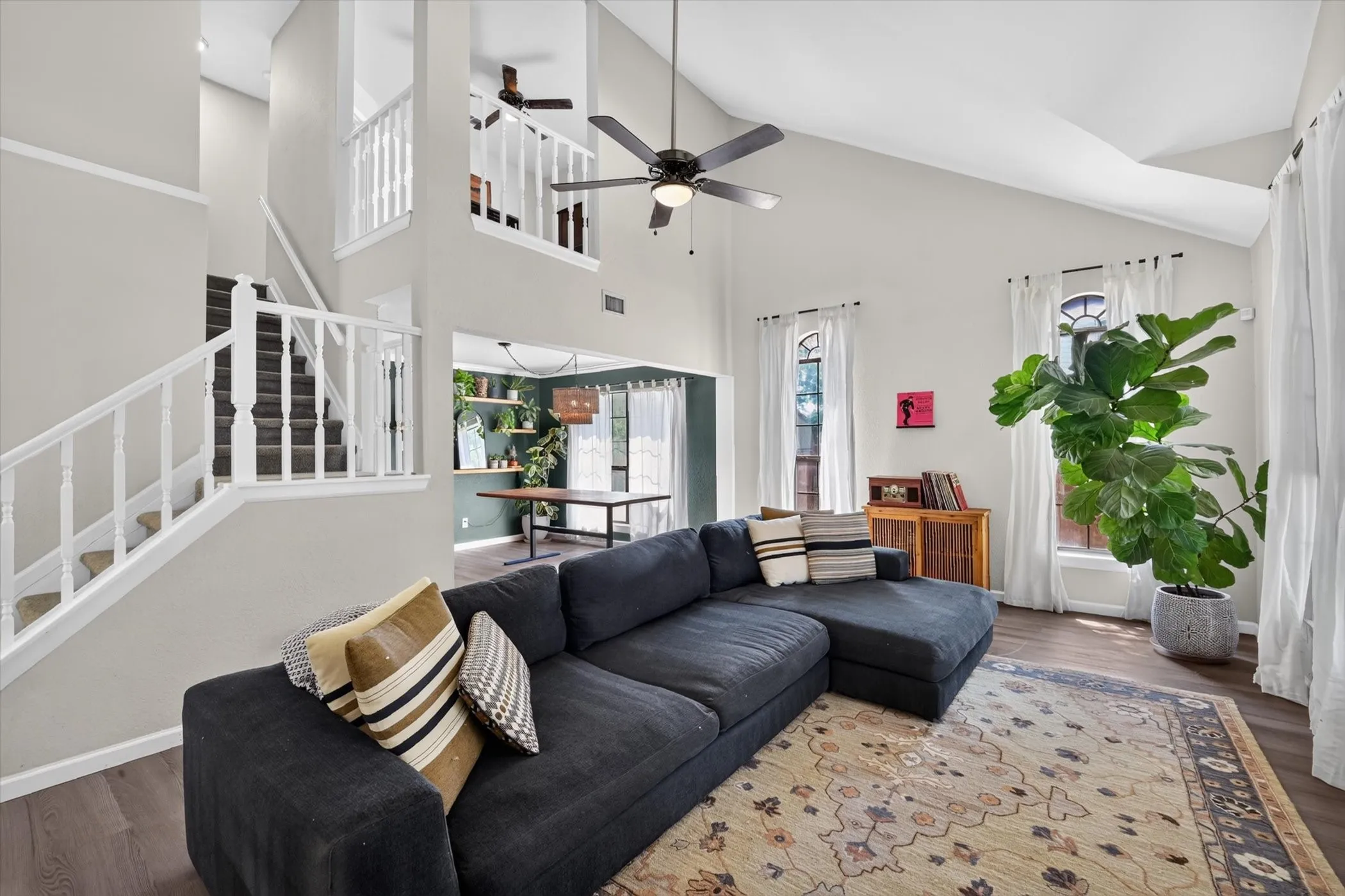 Vaulted ceiling with a ceiling fan, wood-finish flooring, staircase with white balusters, and a second-story landing with a white baluster railing