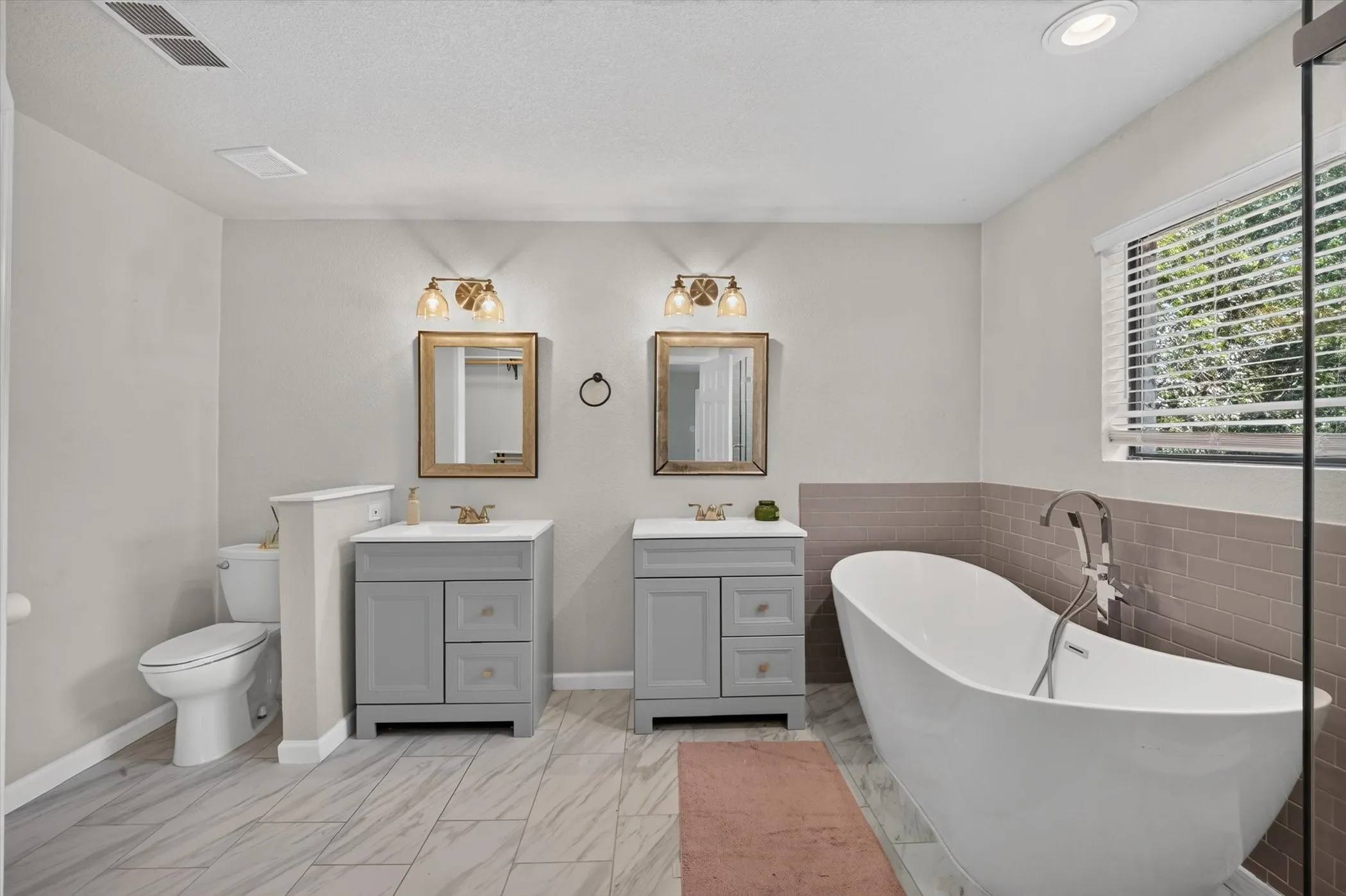 Dual vanity sinks, freestanding soaking tub, tiled flooring, horizontal window blinds, and recessed lighting